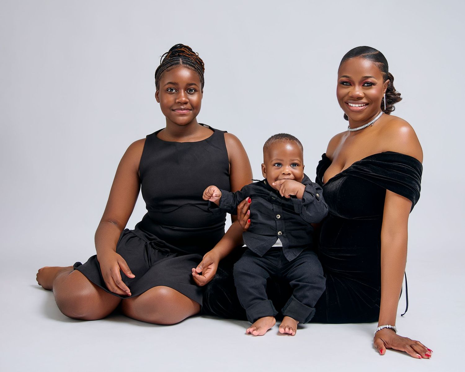 A family wearing matching black outfits poses together laying on the floor in different candid positions.