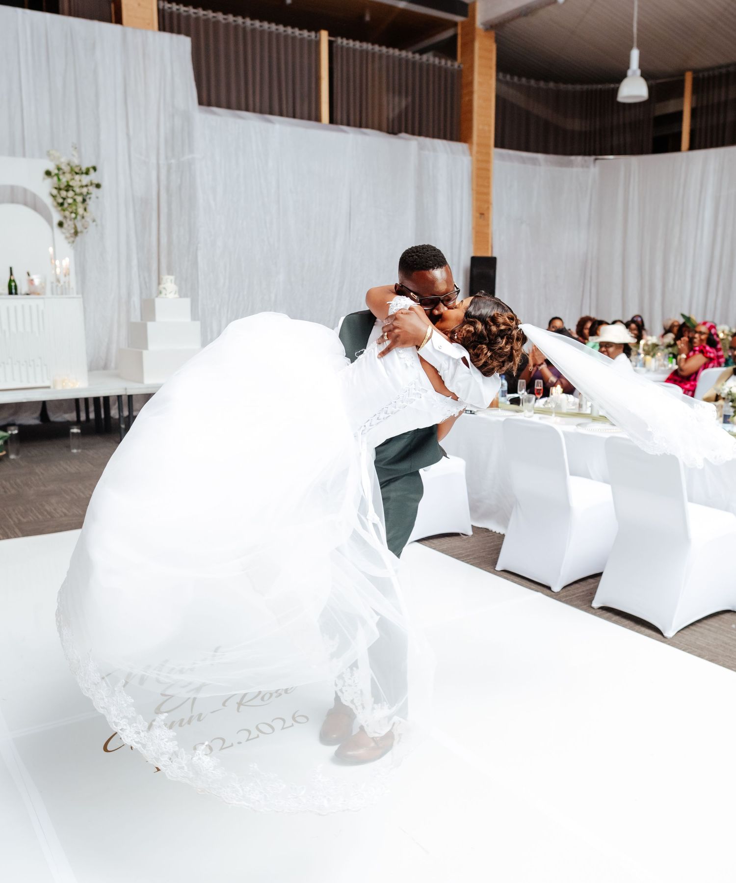 Bride and groom share a romantic dip dance on white dance floor at elegant wedding reception.
