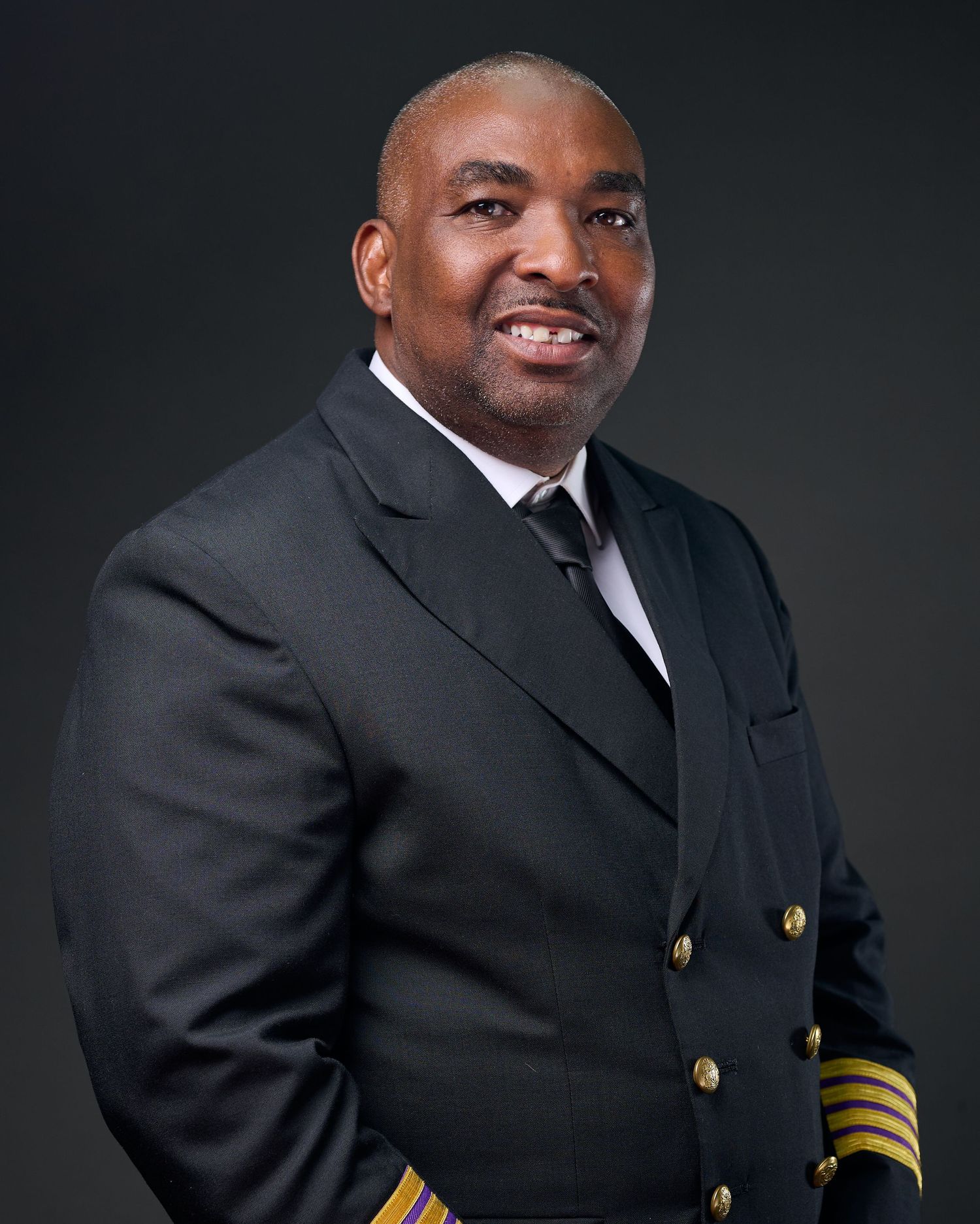Professional headshot of a person in a formal naval officer's uniform with gold stripes against a dark background.