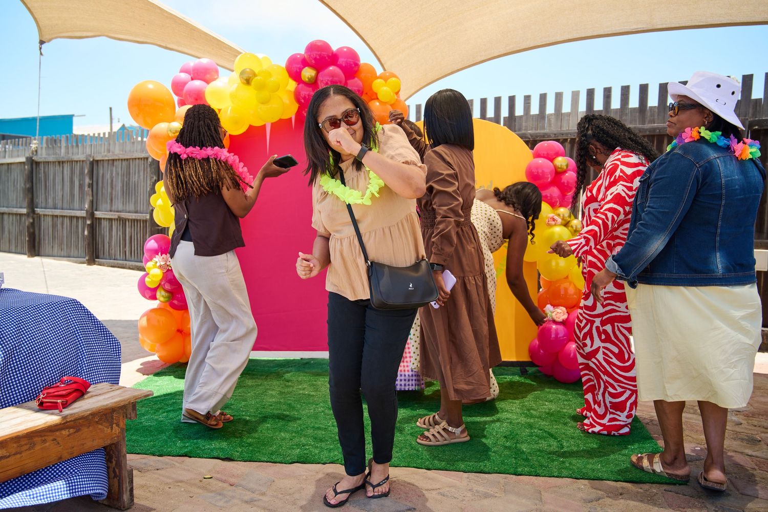 Woman taking a selfie at a colorful tropical outdoor party with balloon arch decor.