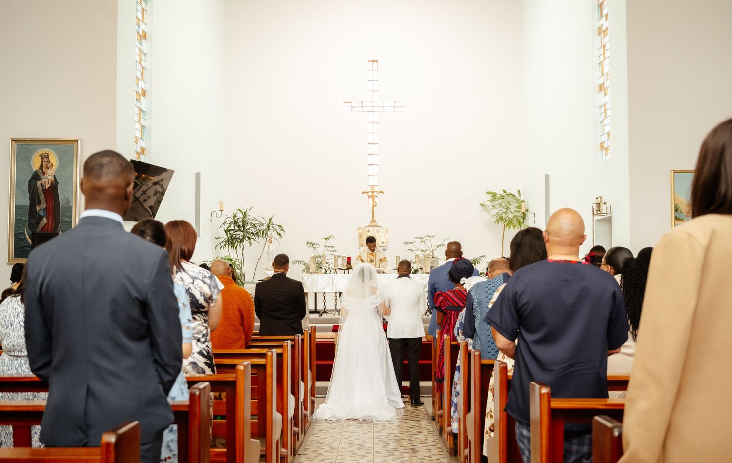 Wedding ceremony in a church with bride and groom at the altar, guests seated in wooden pews.