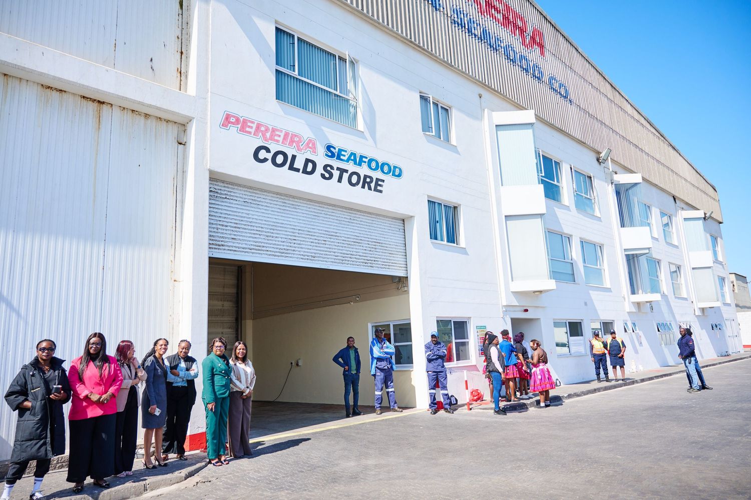 Group of people standing outside Pereira Seafood Cold Store warehouse facility on a sunny day.