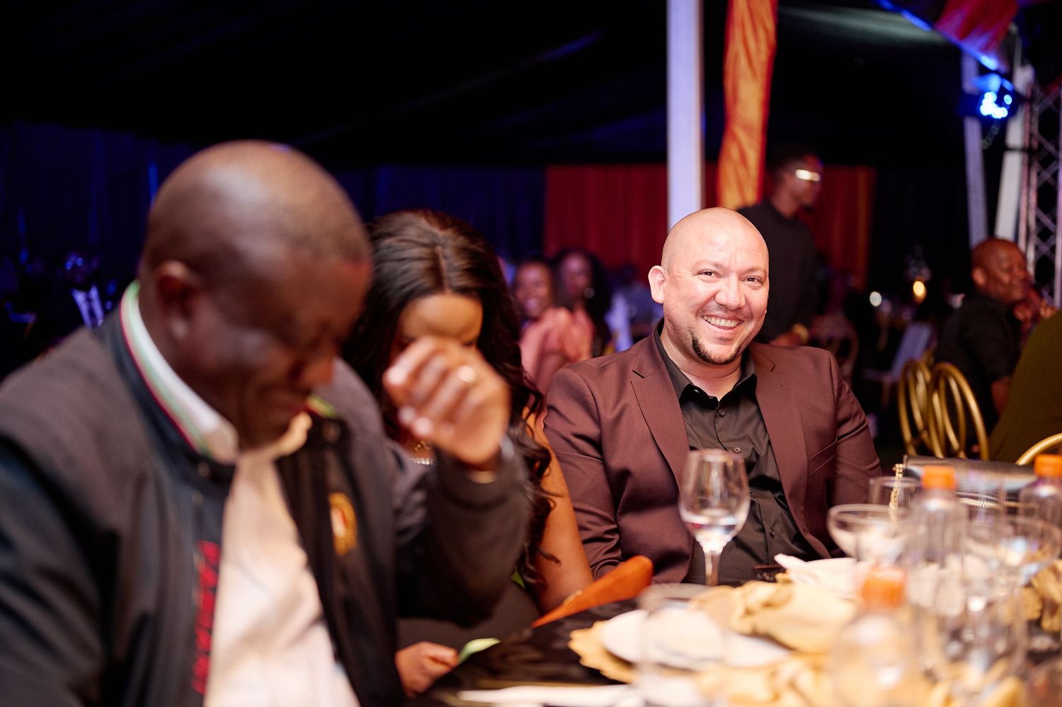 People laughing and socializing at an elegant gala dinner event with festive lighting and table settings.