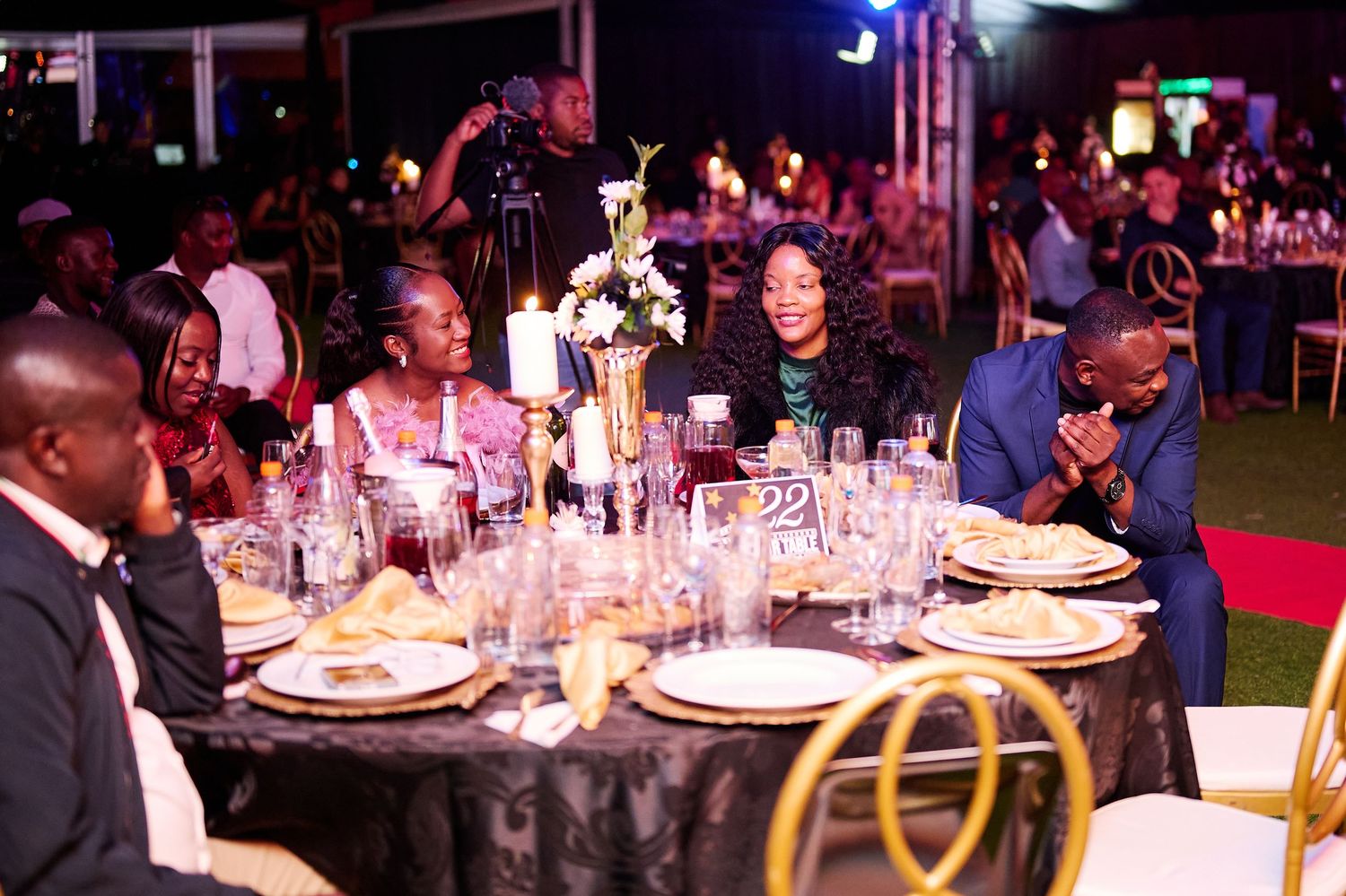 Elegant gala dinner event with guests seated at decorated round tables with floral centerpieces in an outdoor venue.