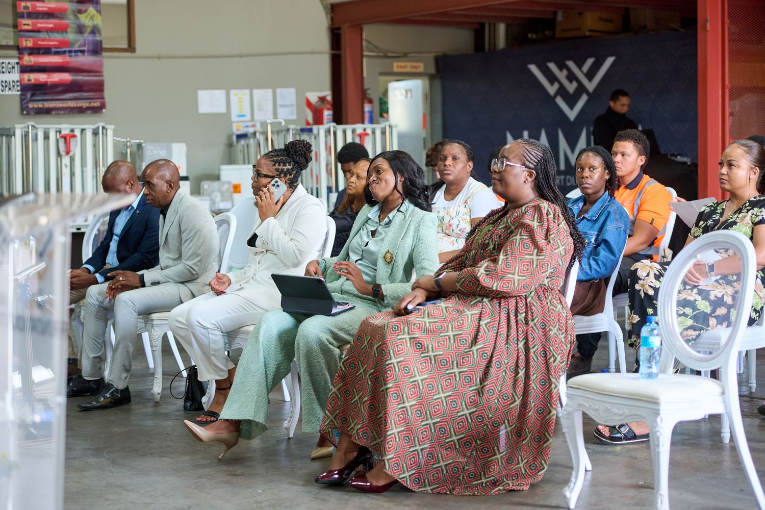 A diverse group of people seated in chairs at an indoor community event or meeting in a modern venue.
