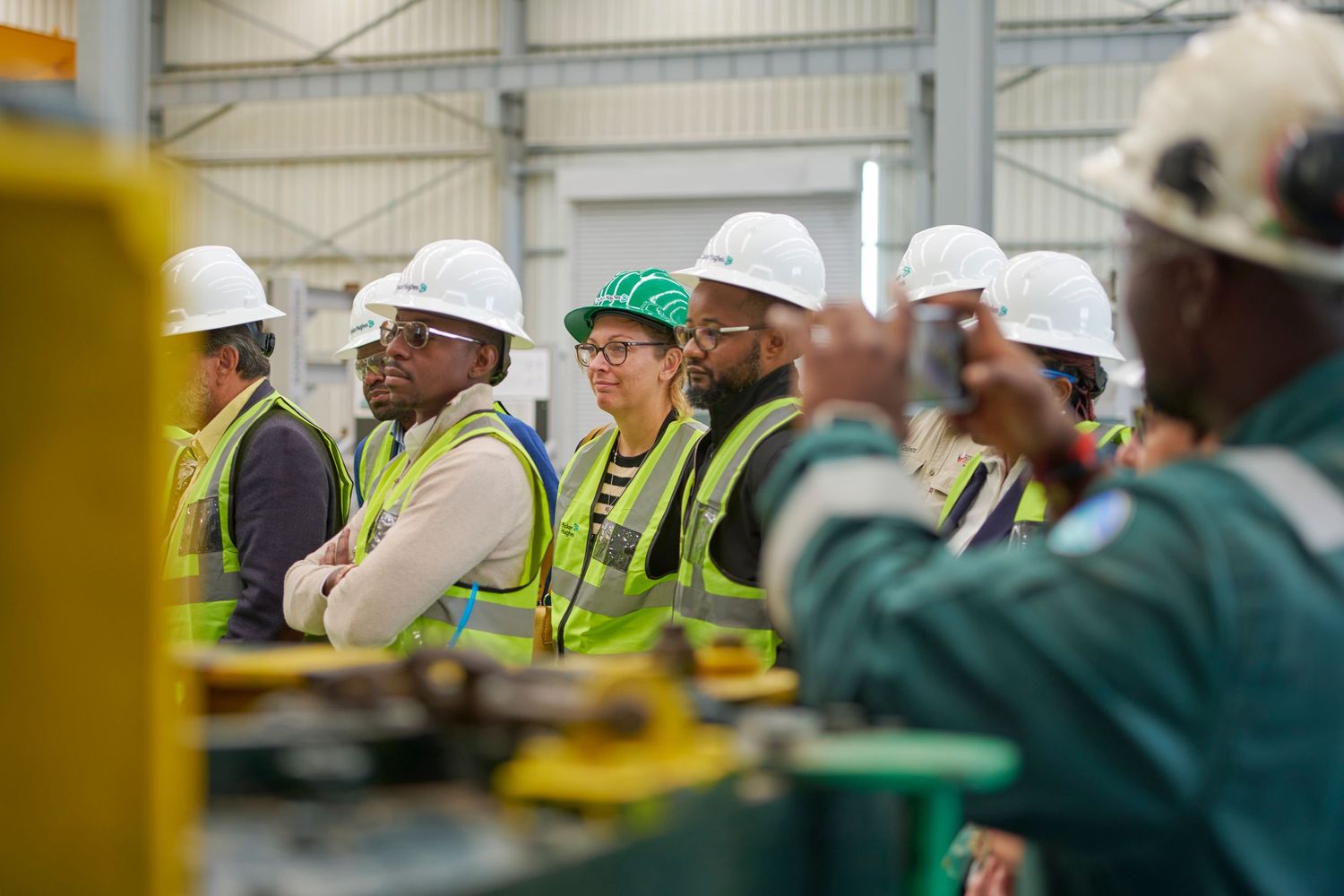 Workers in hard hats and safety vests tour industrial facility during group walkthrough.