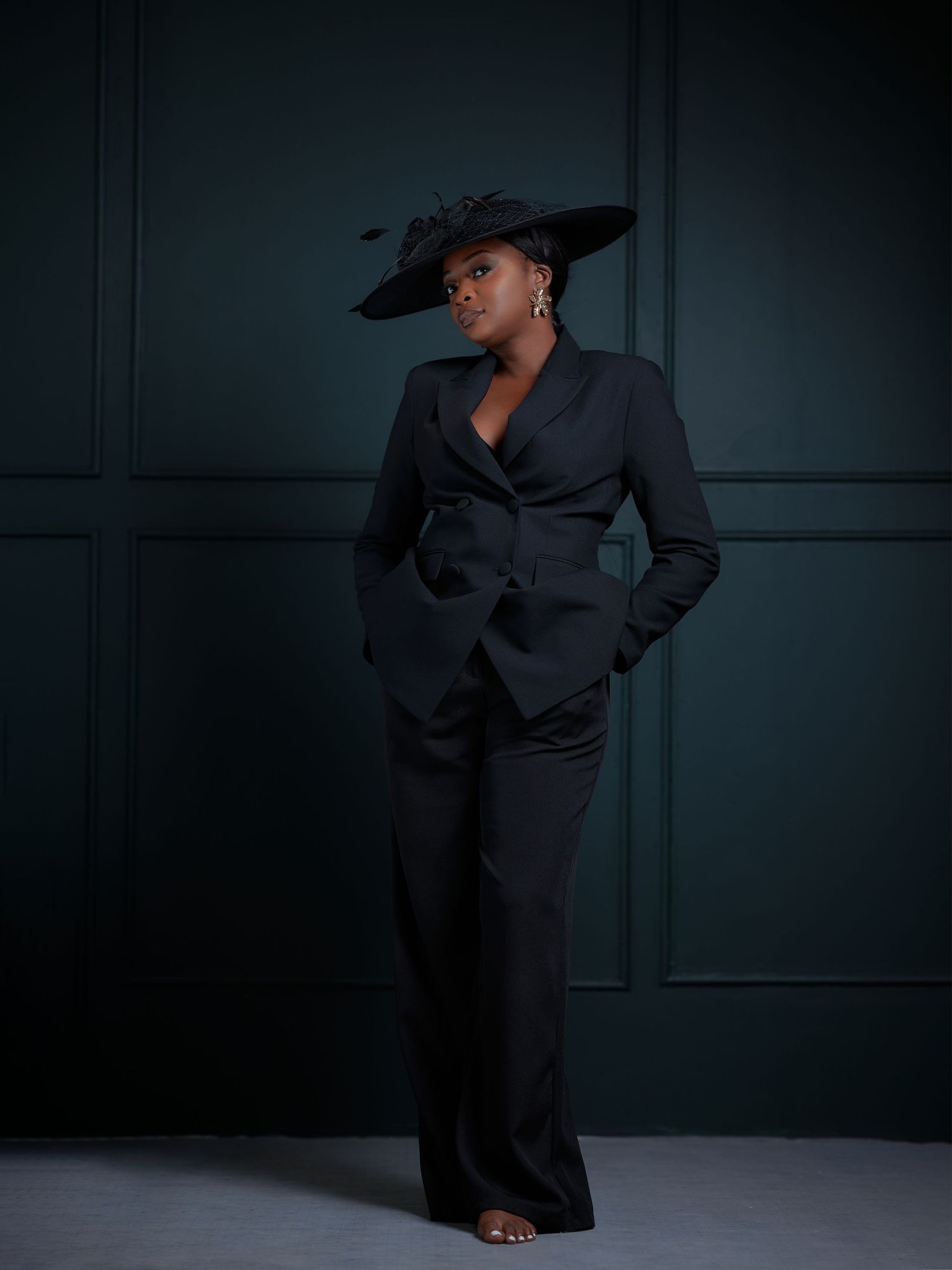Fashion model in black suit poses dramatically against dark backdrop in artistic photoshoot series.