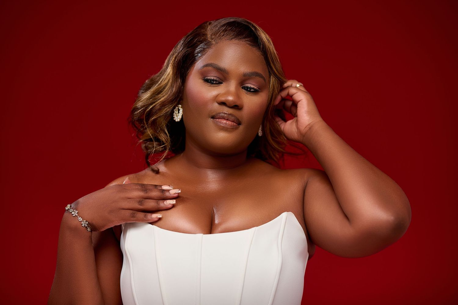 A plus-size woman in a white strapless dress poses gracefully against a bold red background.