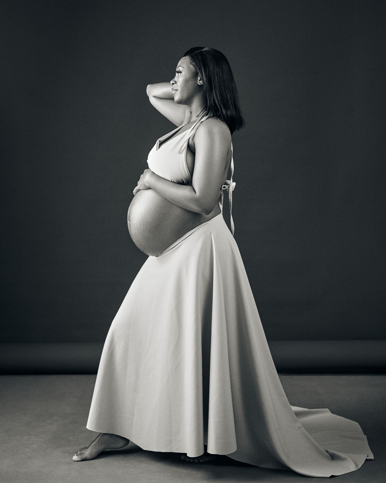A series of black and white maternity photos showing an elegant white dress flowing against a dark background.
