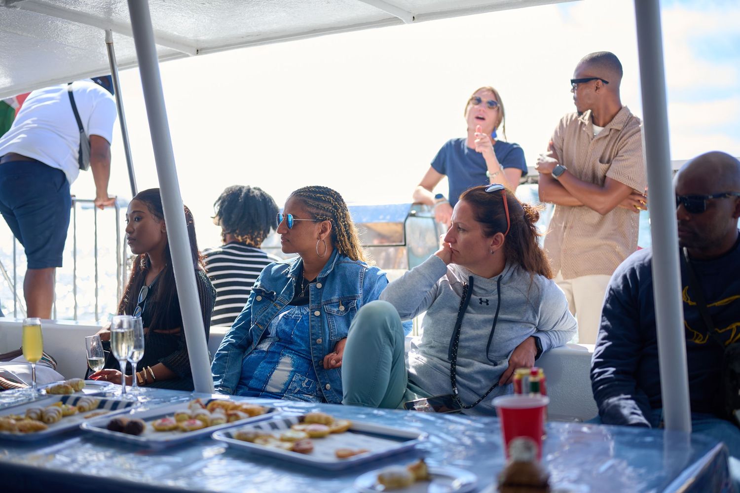 Group of diverse friends enjoying food and drinks on a sunny boat party cruise on the water.