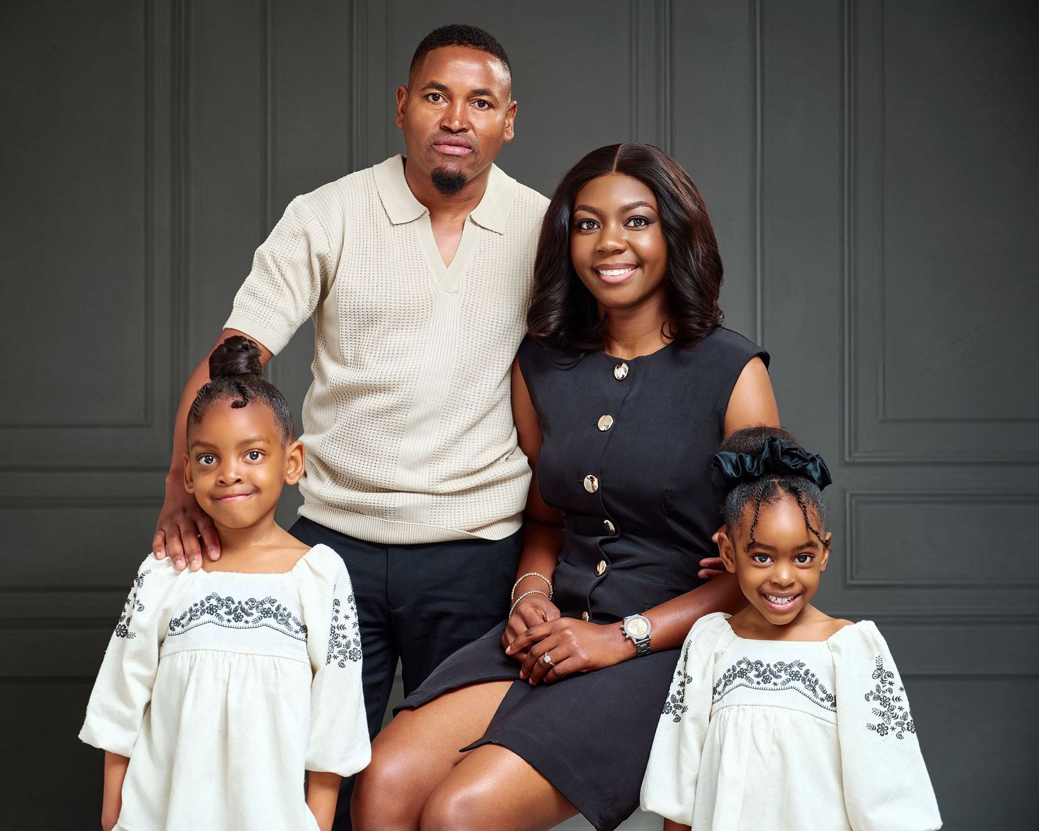 A family of four poses for a portrait, with two parents and two young girls in matching white dresses.