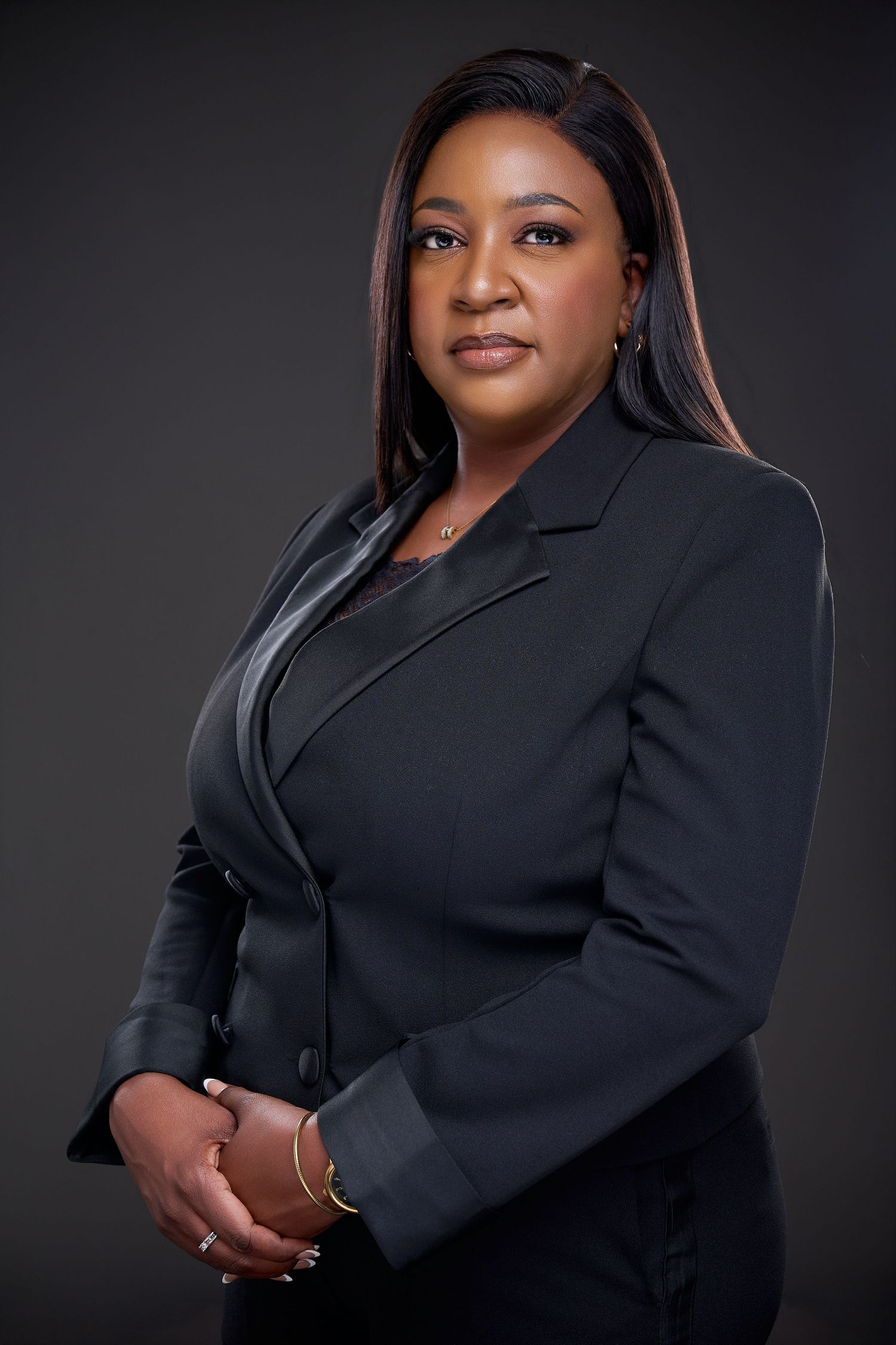 Professional woman in black blazer poses confidently against dark background in formal business portrait photo.