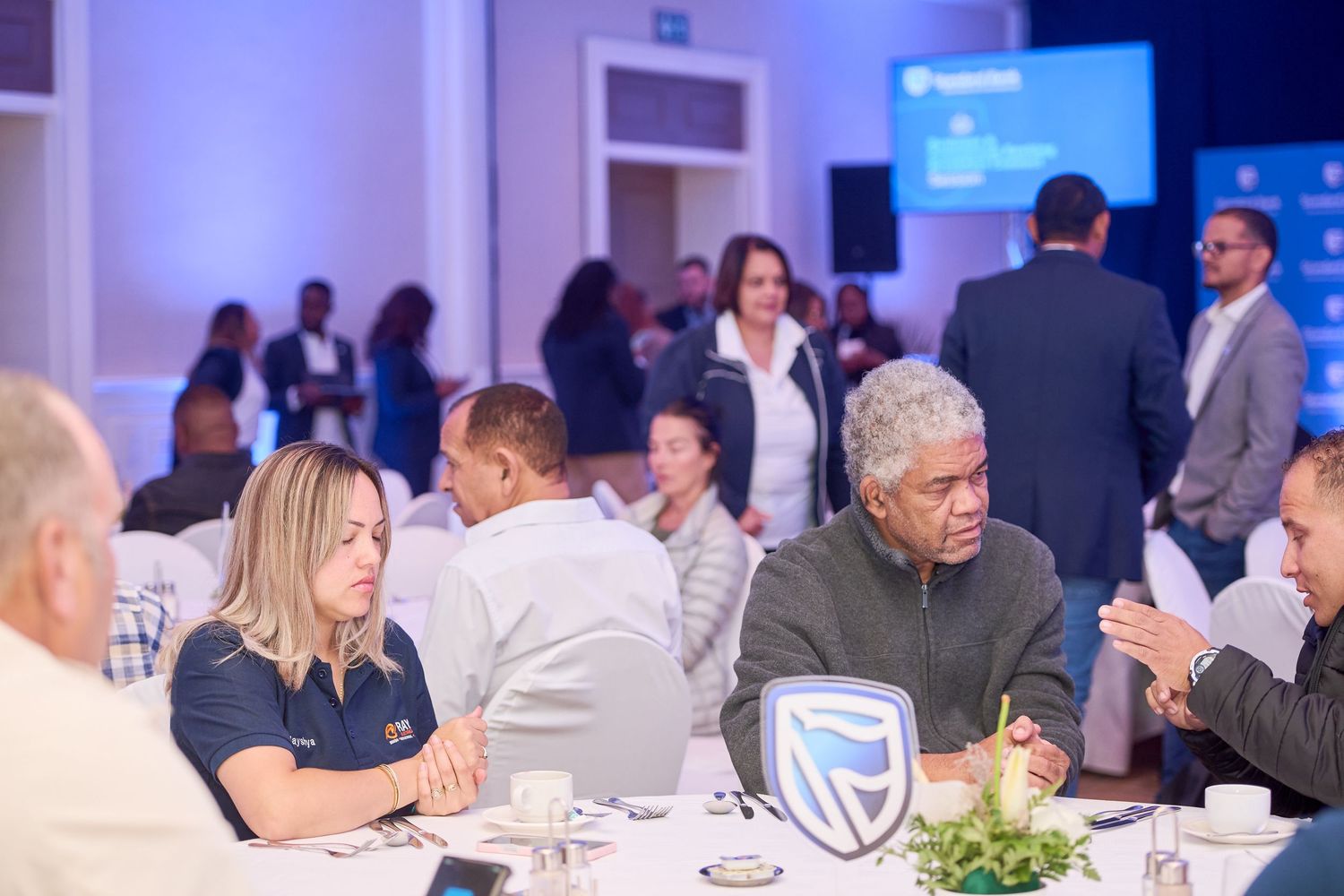 Professionals networking at a corporate event, seated at round tables with Standard Bank branding in an elegant conference venue.