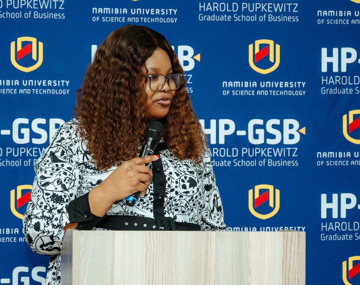 Woman speaking at podium at Namibia University of Science and Technology Harold Pupkewitz Graduate School of Business event.