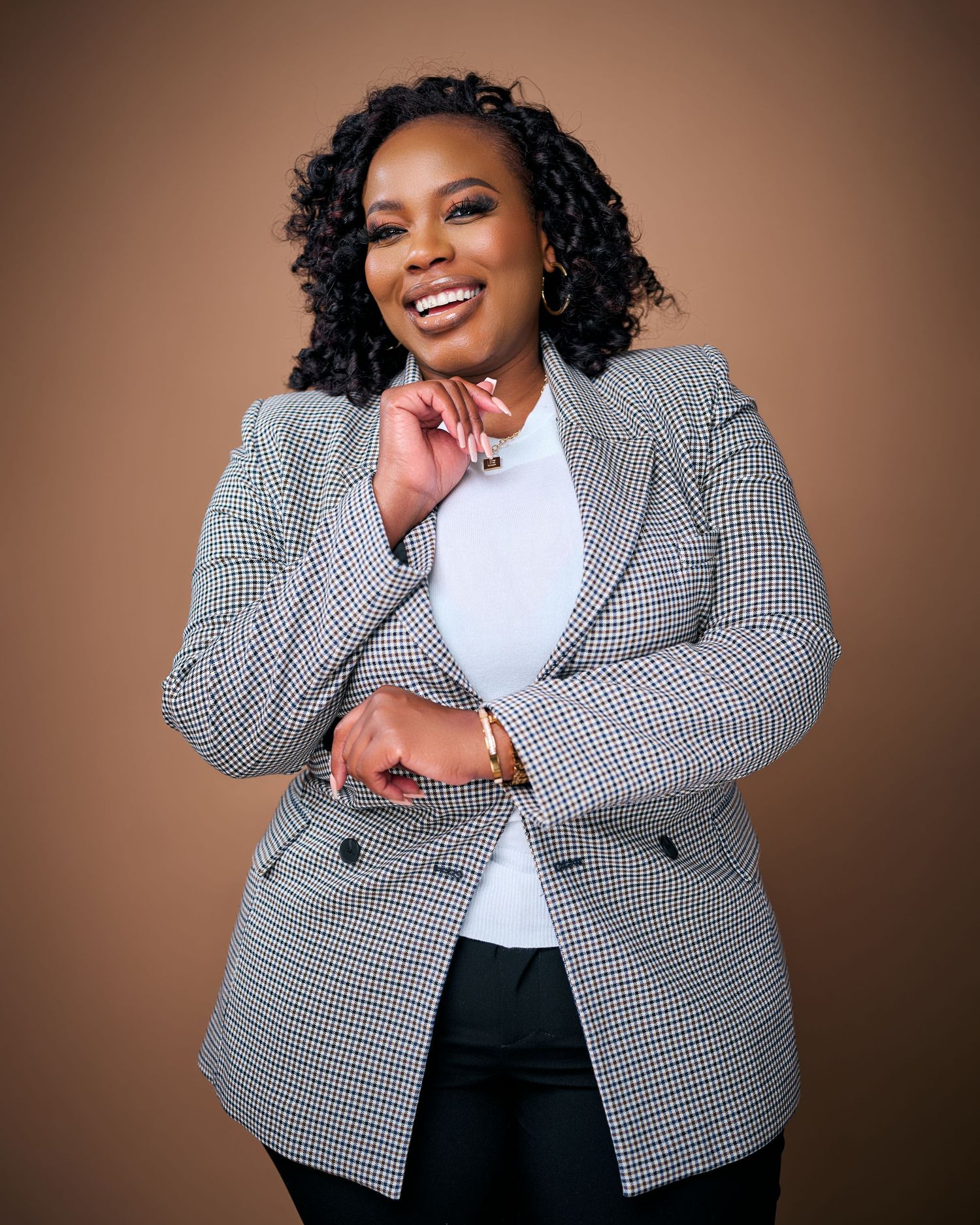 A person wearing a black and white houndstooth blazer and white top poses expressively against a brown background.