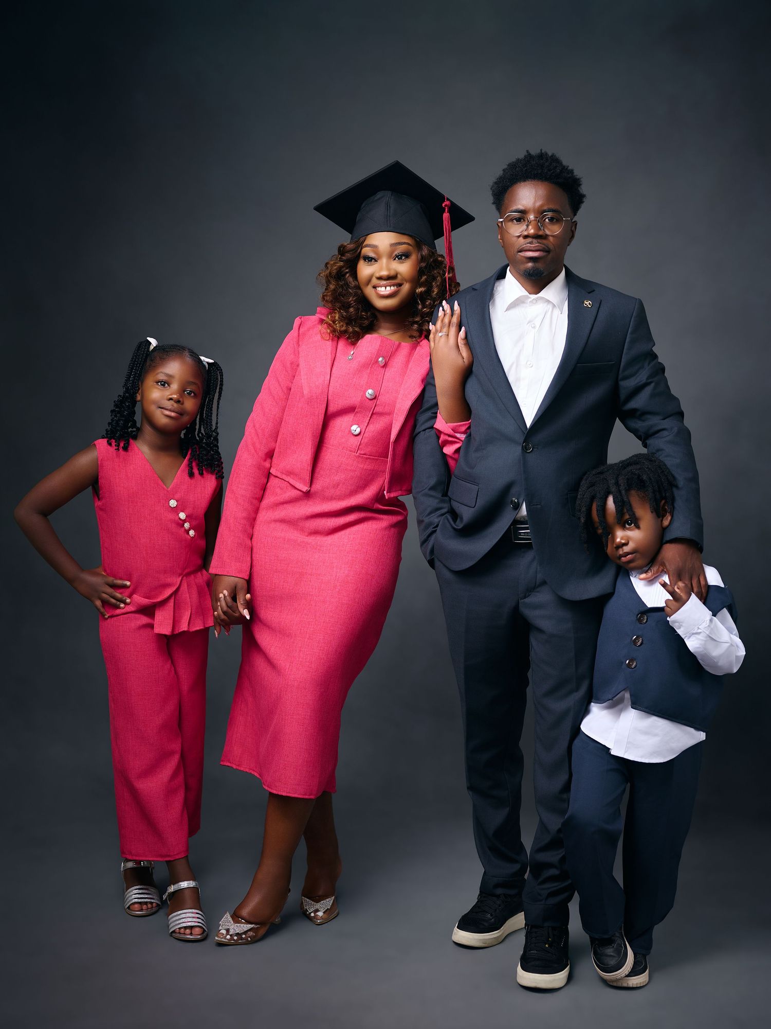 A woman in pink graduation attire poses with three children for a celebratory family portrait.