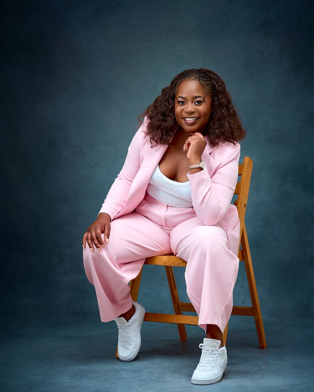 Professional studio portrait featuring a pink pantsuit and white sneakers against a dark moody backdrop.