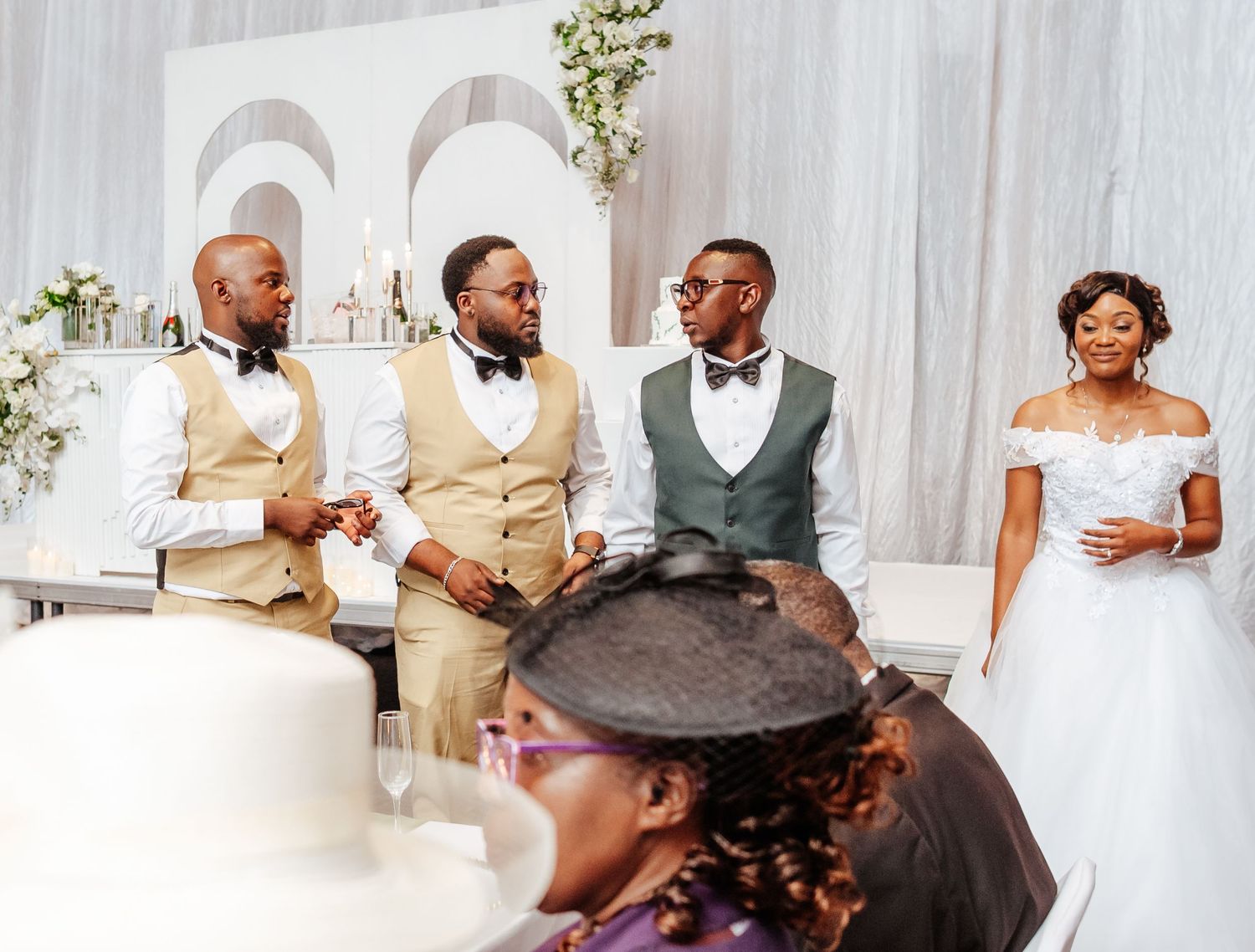 A bride in white stands with three groomsmen in tan vests at an elegant wedding ceremony.
