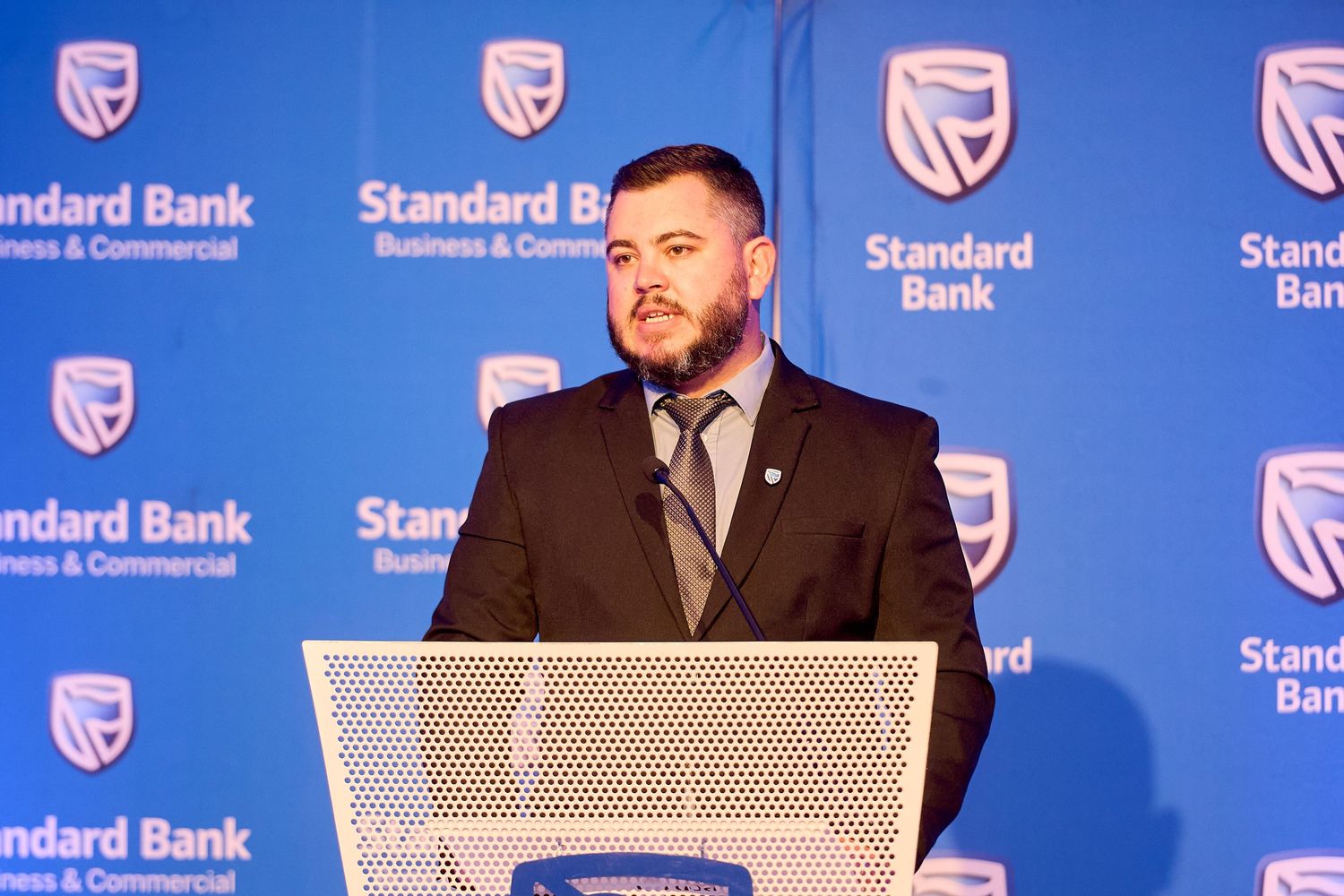 Man in suit speaking at Standard Bank Business & Commercial podium at a formal corporate event.