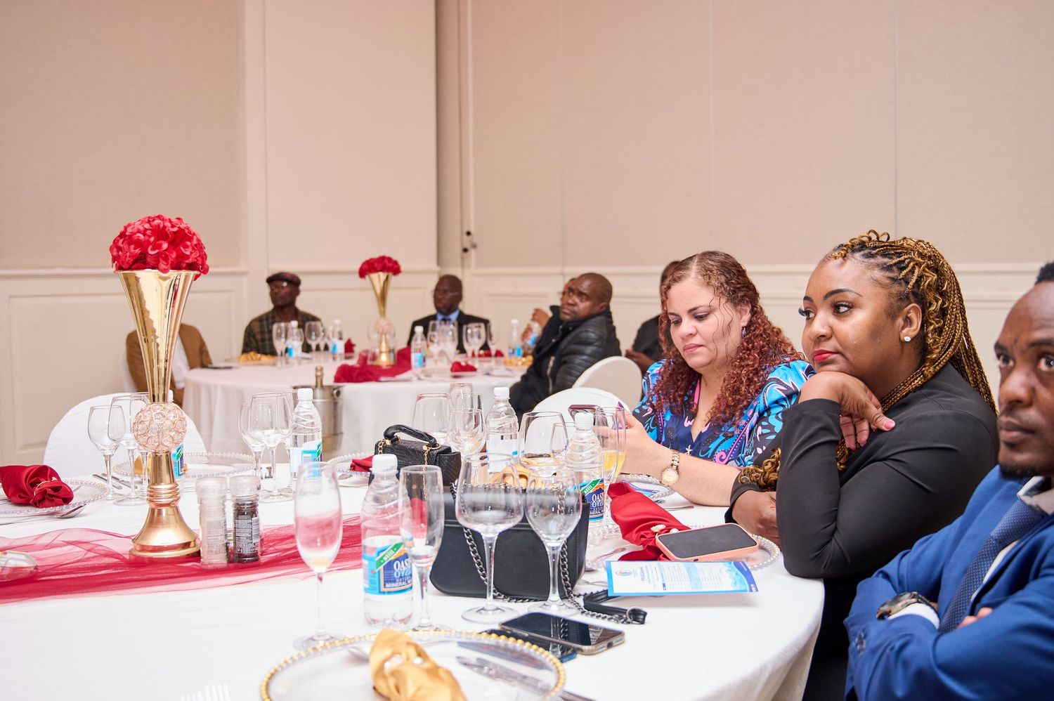 Guests seated at elegantly decorated banquet tables with red floral centerpieces during a formal event.