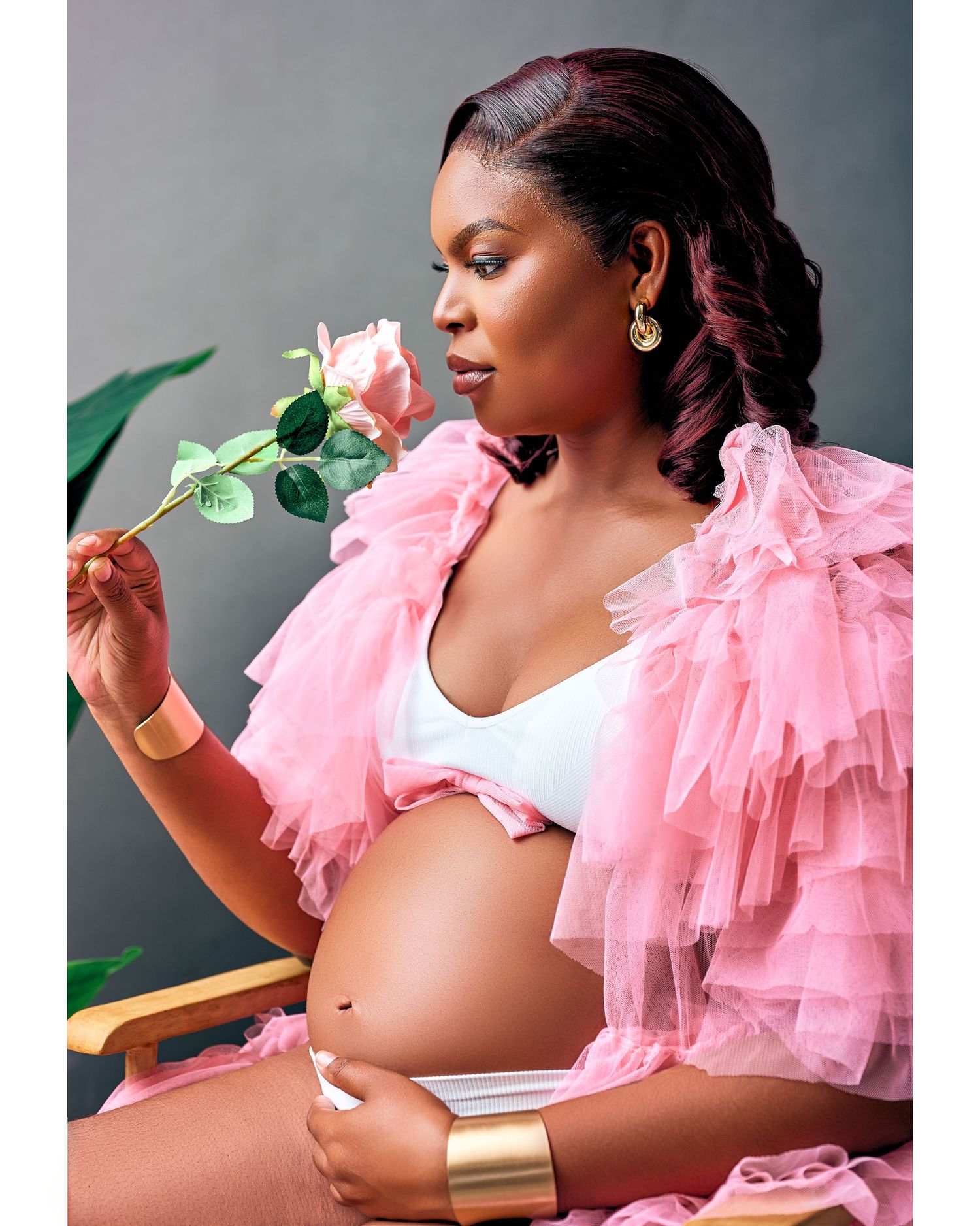 A side profile portrait in pink ruffled tulle with a delicate rose stem against a gray backdrop.