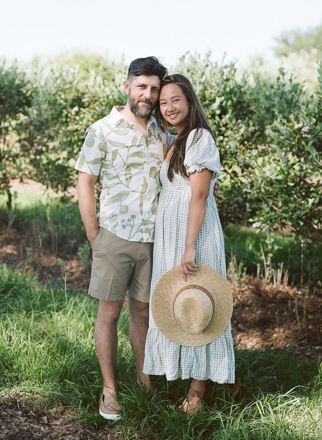 Romantic couple shares tender moments in a garden setting wearing coordinated beige and white summer outfits.