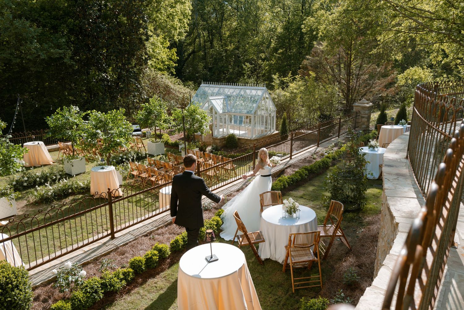 A scenic outdoor dining terrace with white tablecloths and chairs overlooking a lush garden landscape at sunset.