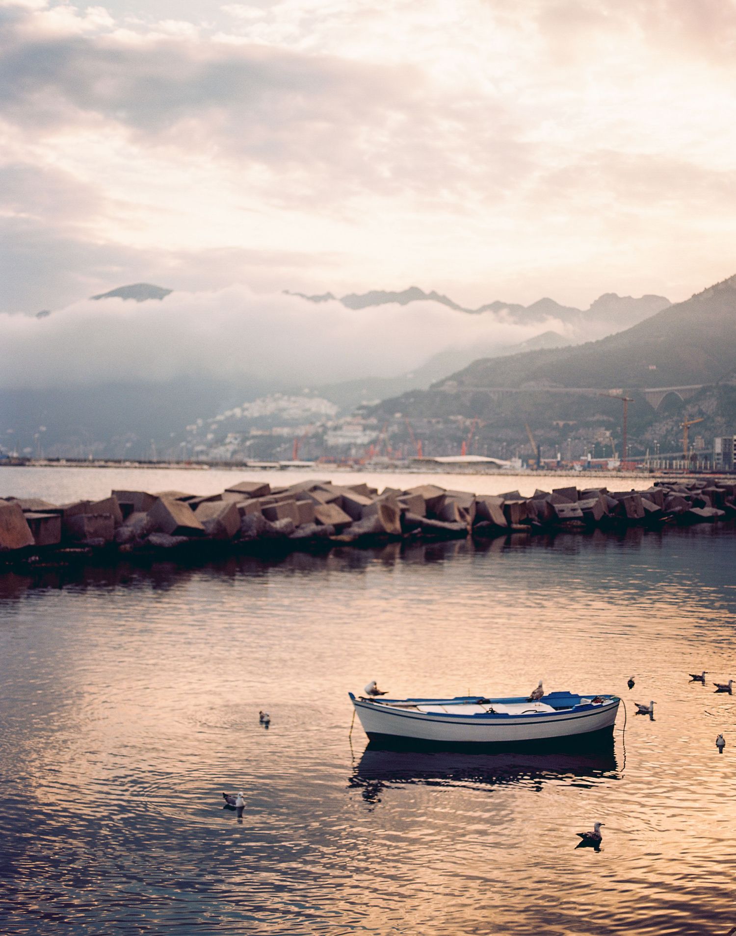 A panoramic sequence of a tranquil harbor at sunset with boats silhouetted against the golden water and mountain backdrop.