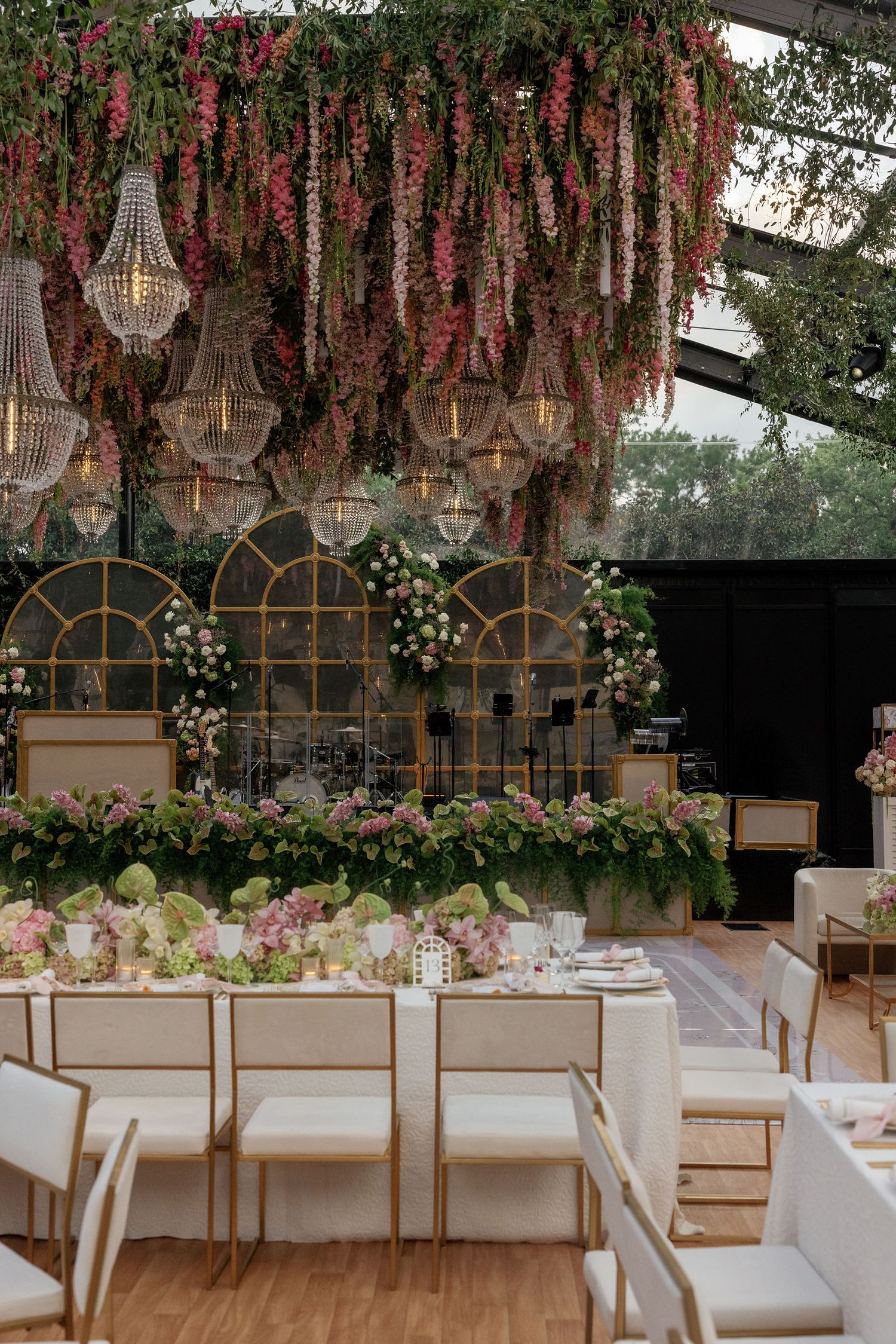 Elegant wedding reception setup with crystal chandeliers, hanging pink flowers and white seating arrangements.