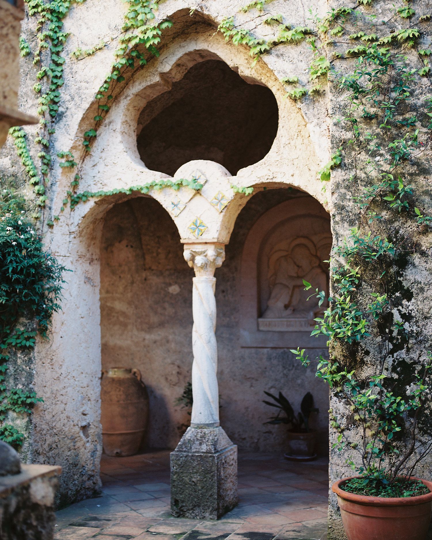 Ancient stone arches with decorative columns and ivy create a serene courtyard atmosphere in a medieval monastery.