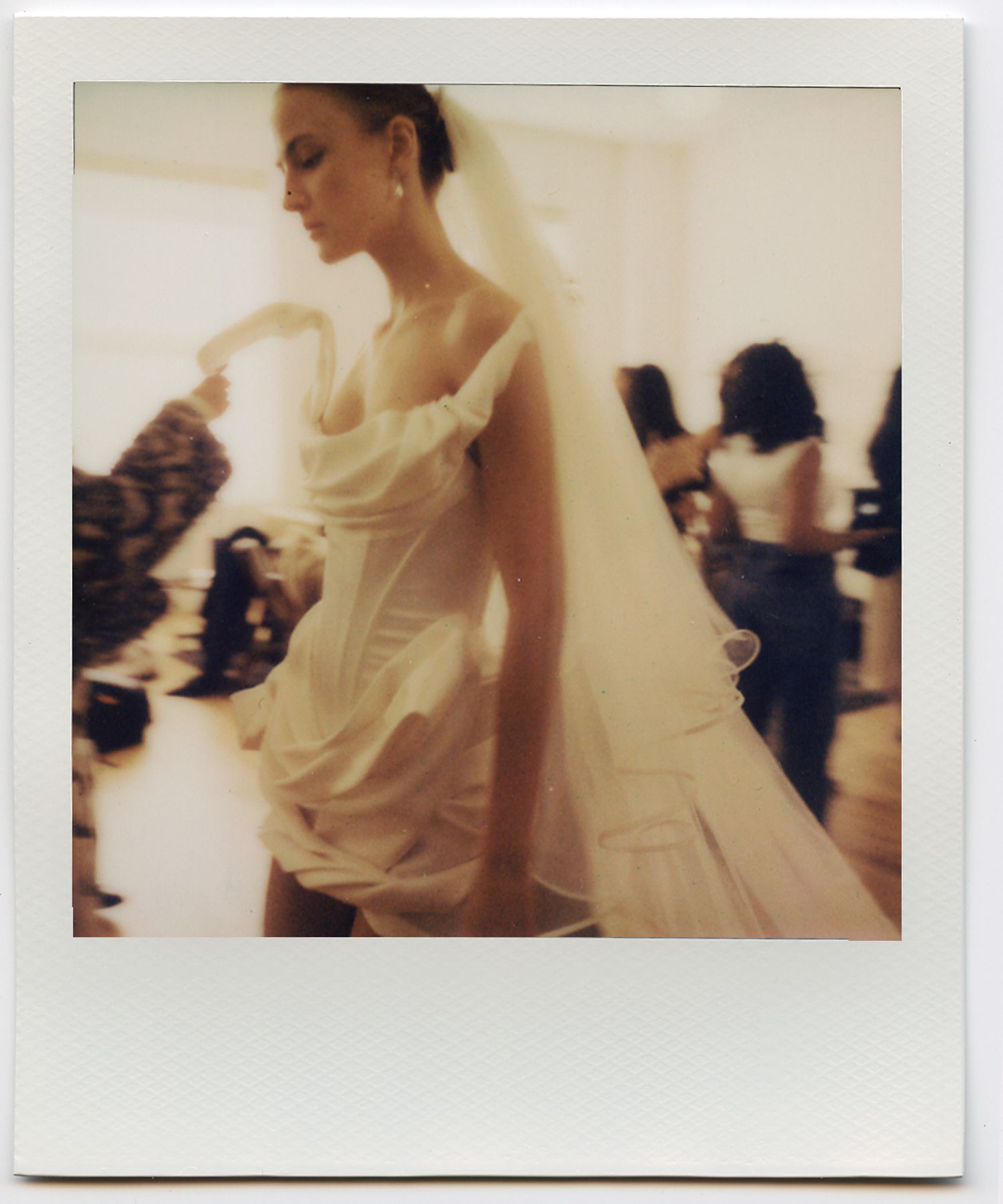 A bride in a flowing white wedding dress and veil poses elegantly in a Polaroid-style photo.