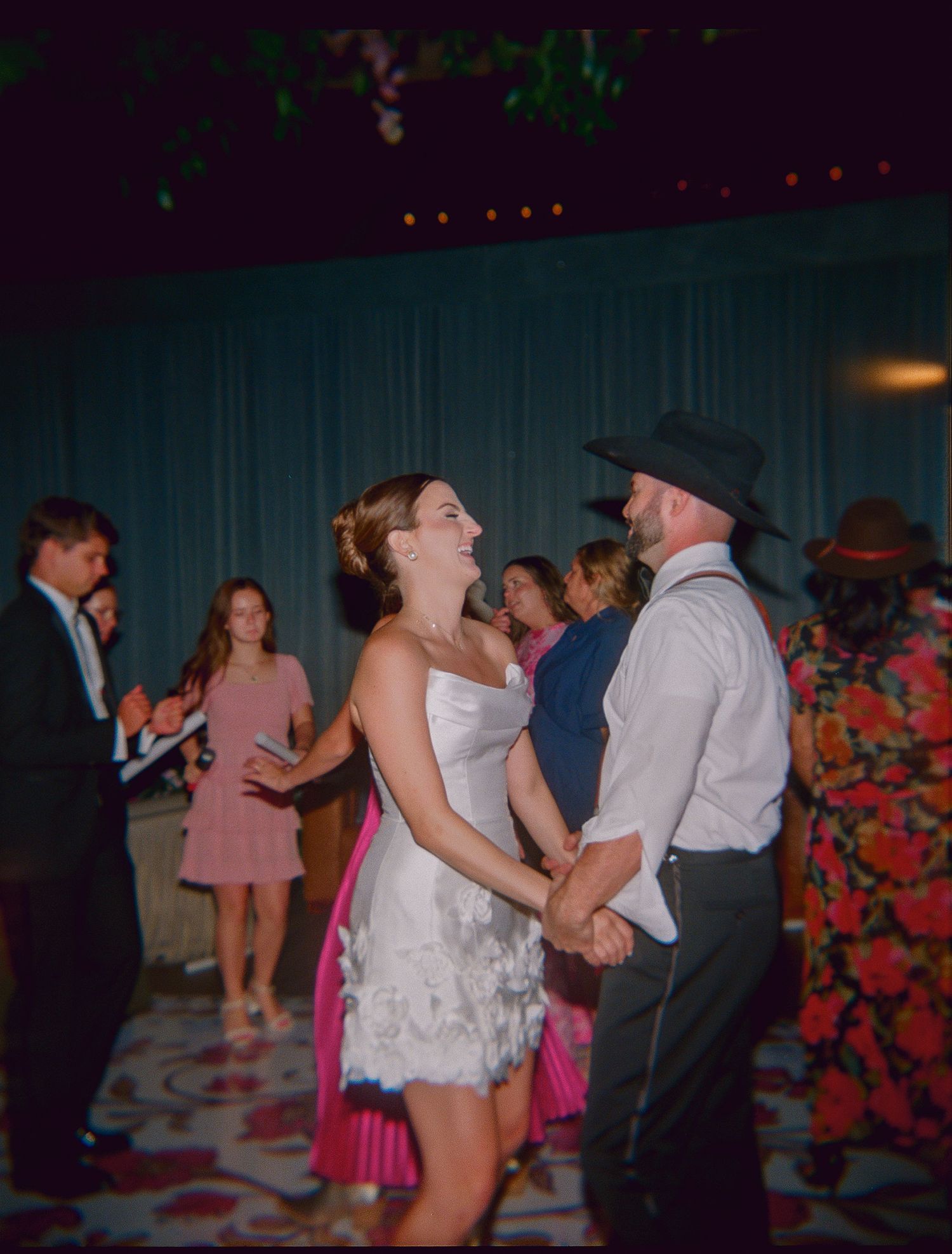 People dancing together at a dimly lit reception party with colorful lights and decorations.
