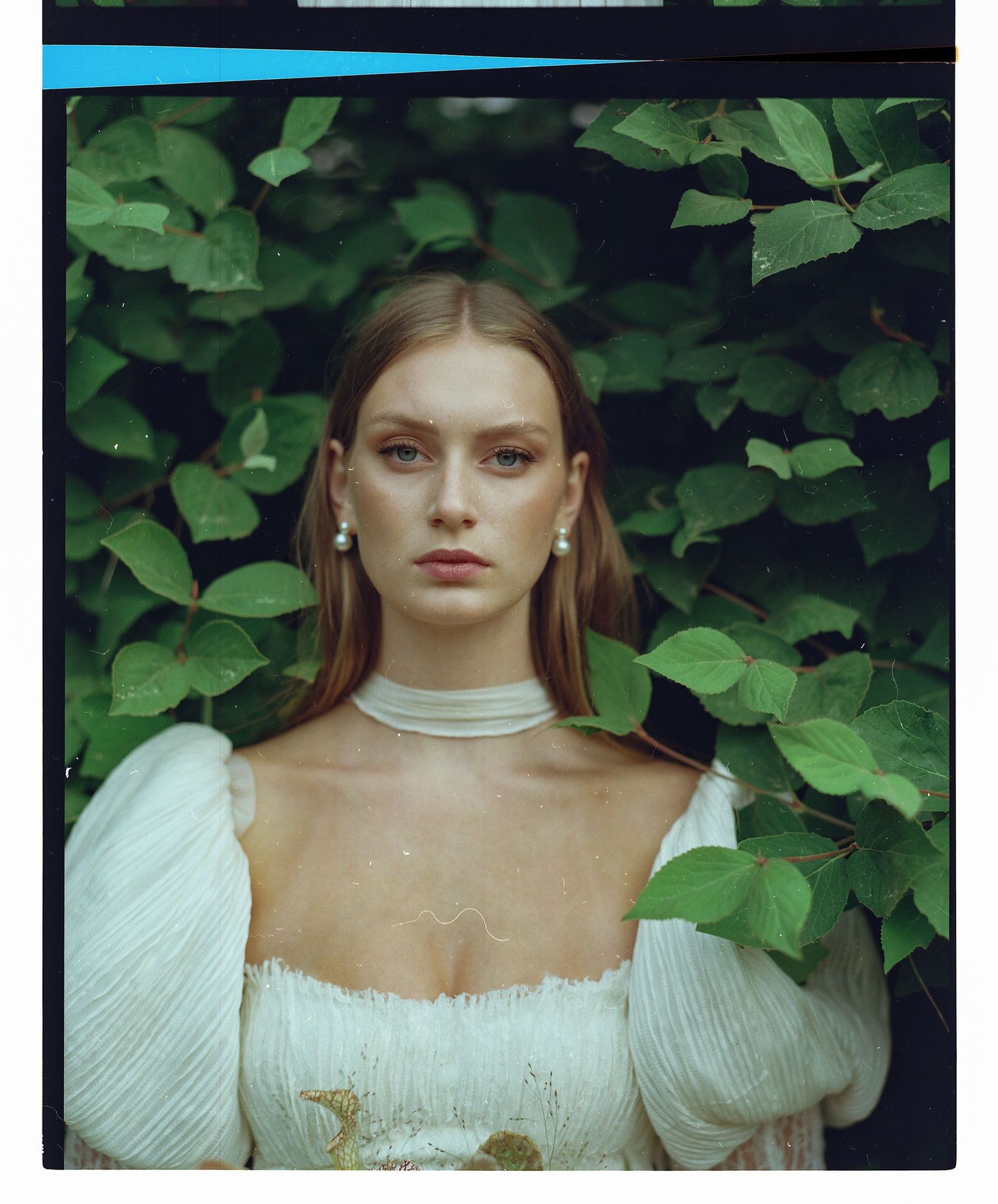 A portrait in a white puffy-sleeved dress against lush green foliage background.