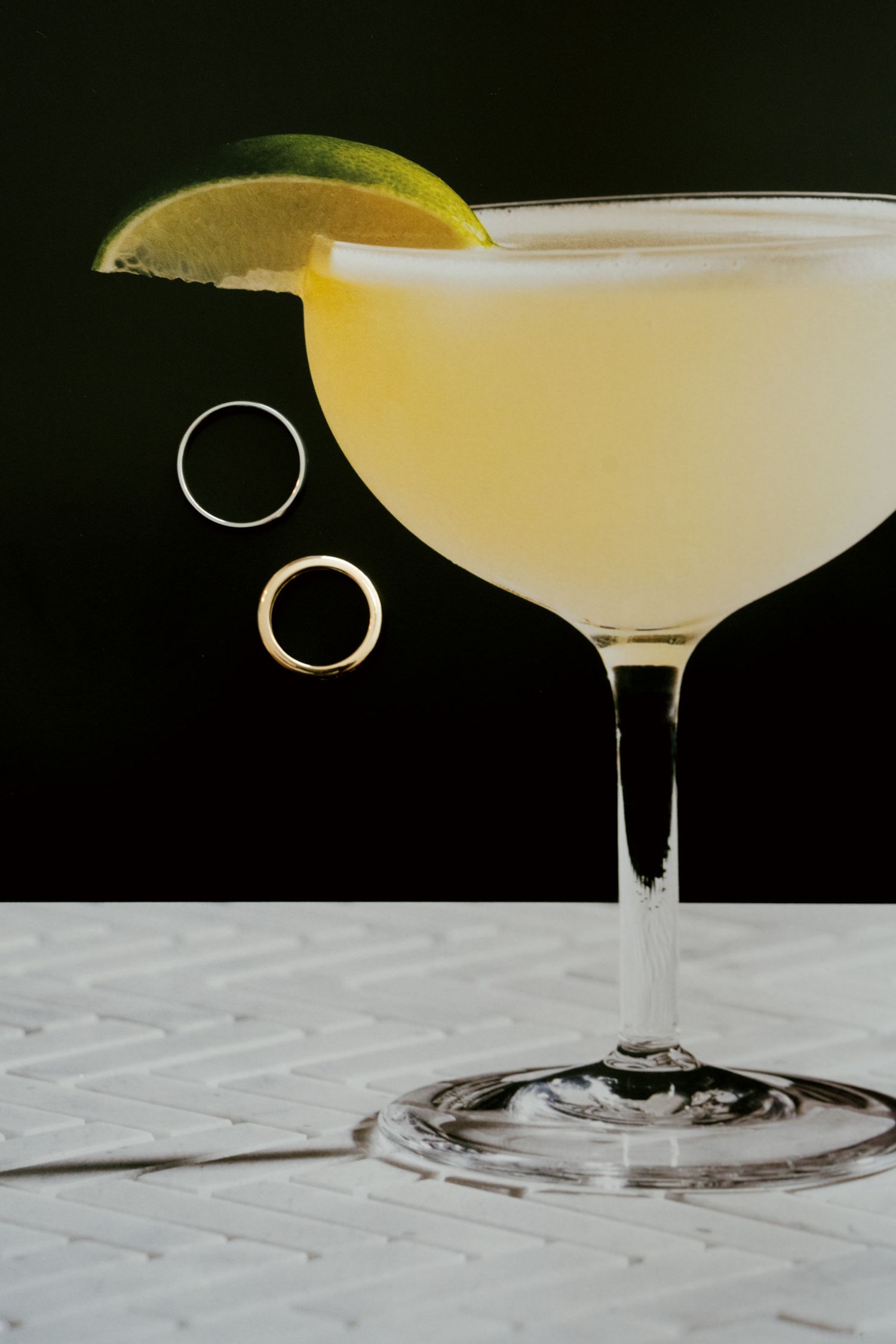 A chilled daiquiri cocktail in a coupe glass with a lime wedge garnish and two rings beside it.
