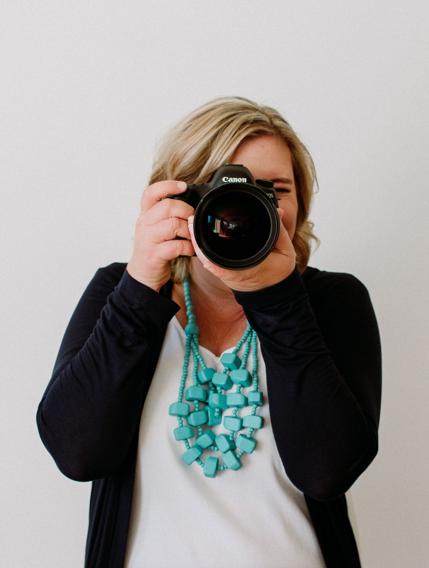 A photographer in a navy blazer and turquoise necklace demonstrates three different camera angles with a DSLR camera.