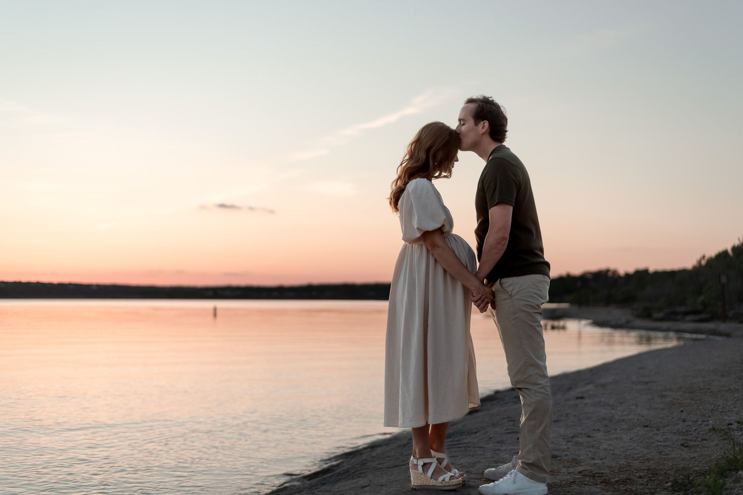 Couple kissing at sunset by the water during romantic maternity photoshoot in Central Texas