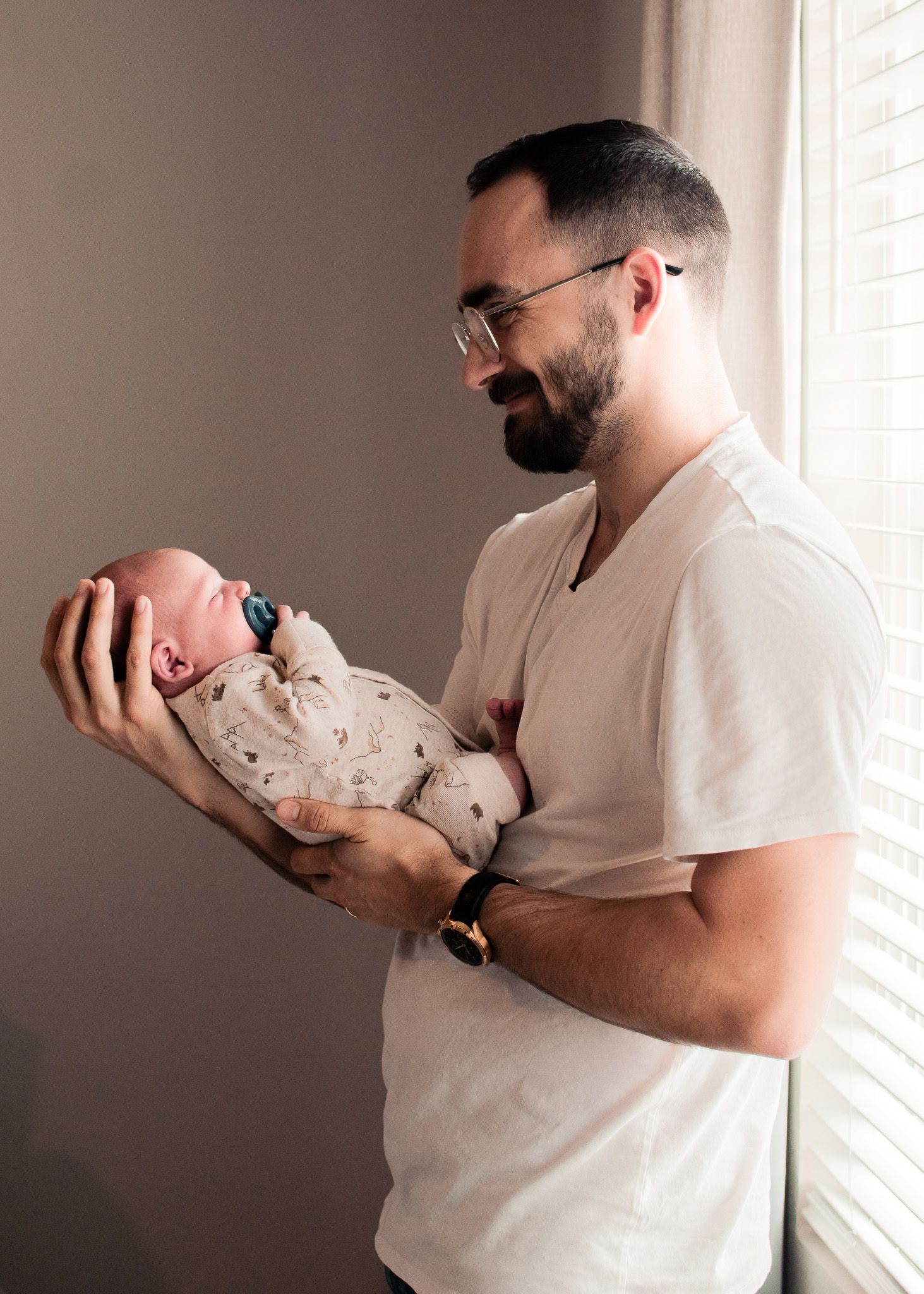 Father holding newborn baby by window during session with a Belton Texas newborn photographer