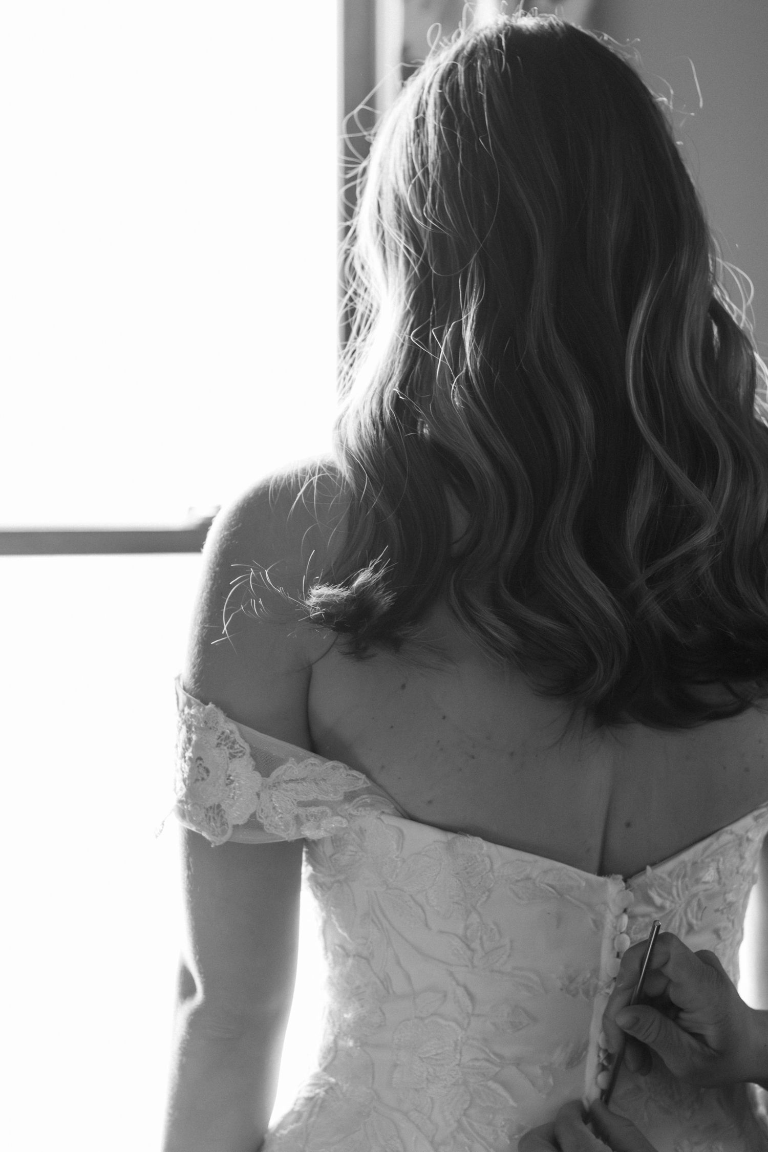 Black and white close-up of a wedding dress being buttoned up.