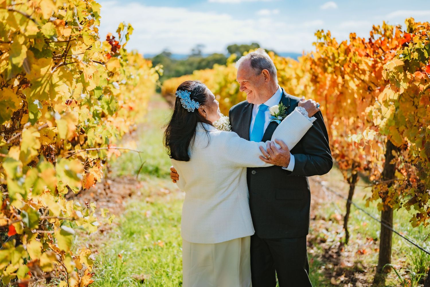 A couple shares a romantic moment while dancing among golden autumn grapevines in a sunlit vineyard.