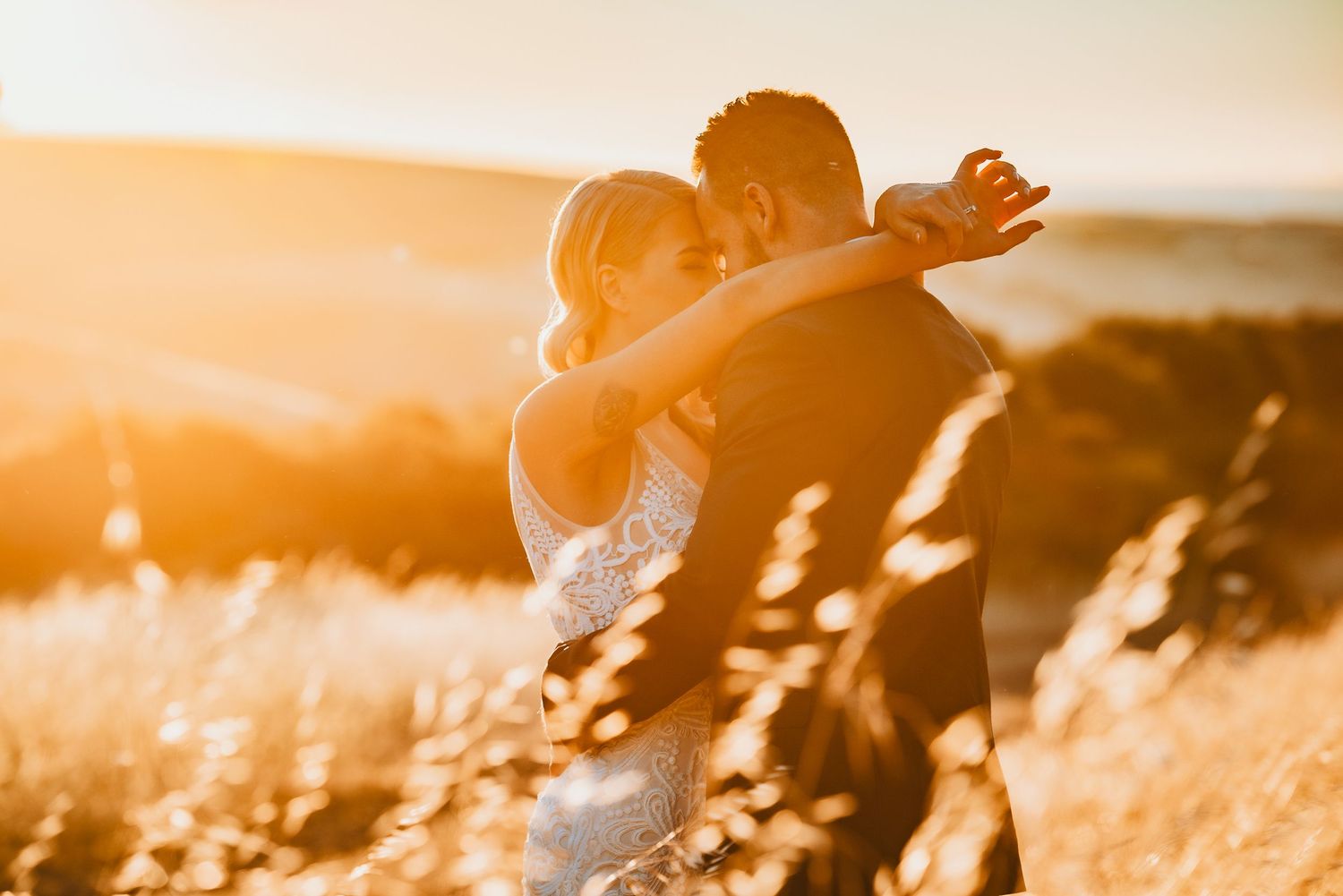 A romantic golden hour embrace in a sunlit field as silhouettes of a couple stand against the warm evening light.