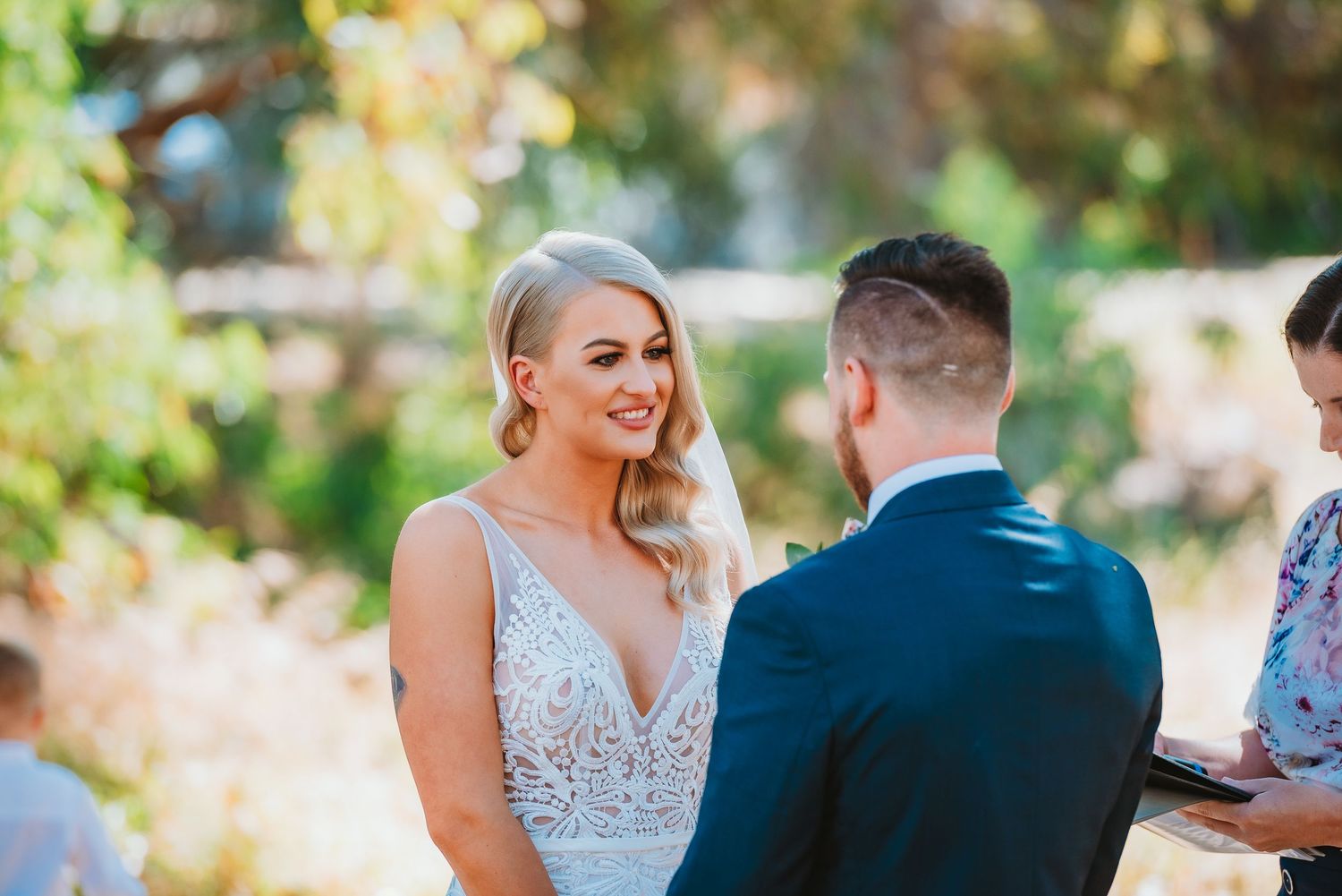 A couple exchanges vows during an outdoor wedding ceremony with beautiful bokeh lighting in the background.