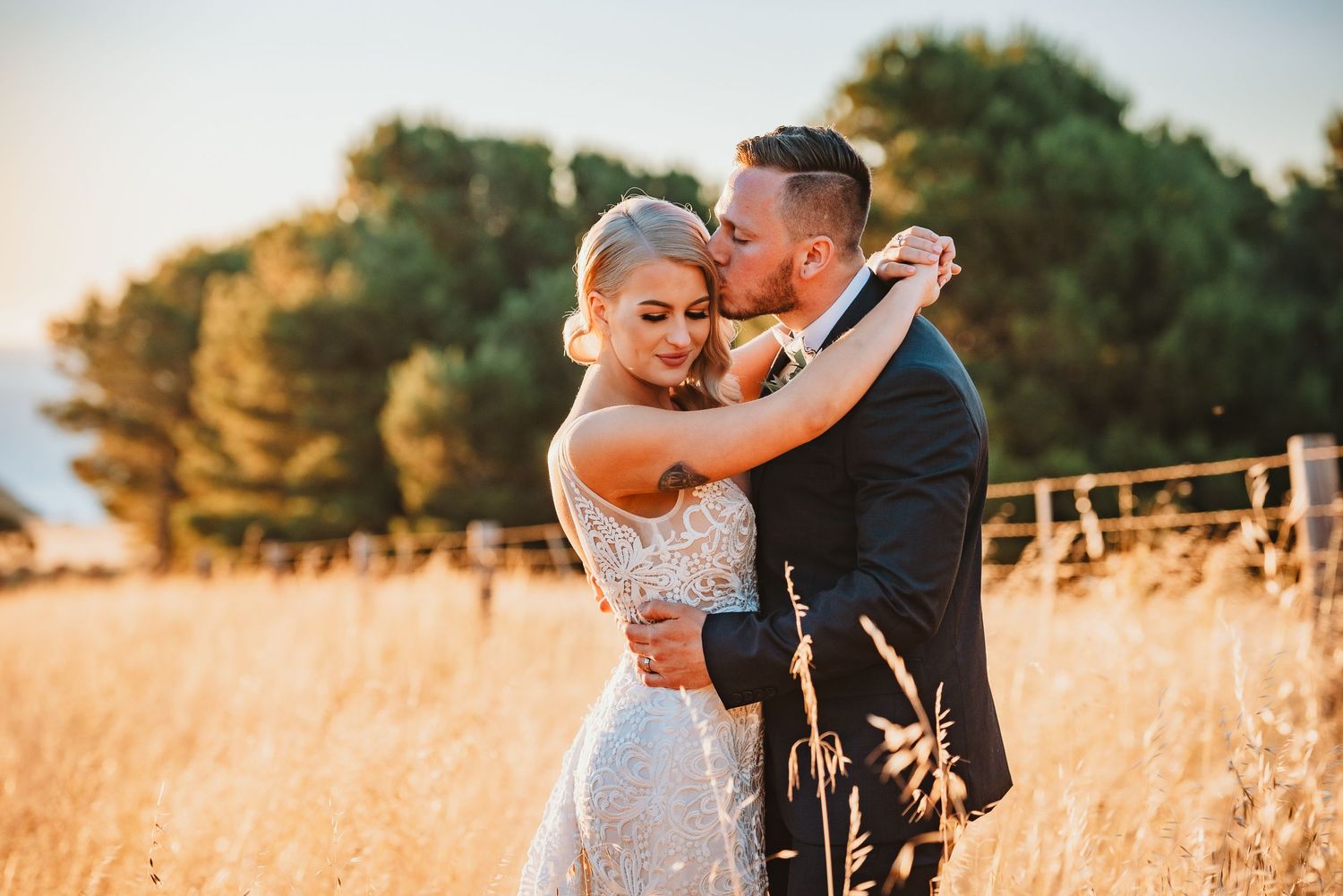 A couple embraces during sunset in a golden wheat field wearing wedding attire.