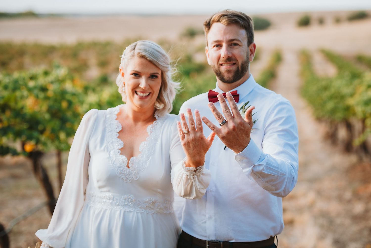 Newlywed couple showing off their wedding rings in a vineyard during golden hour.