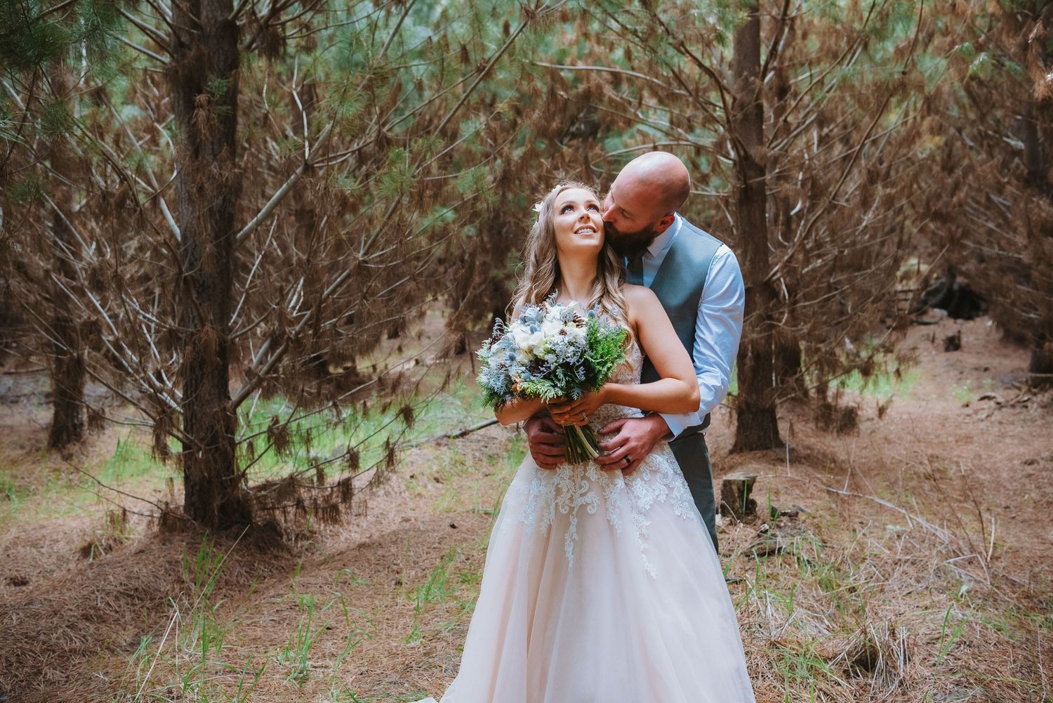 A romantic outdoor wedding portrait of a couple embracing in a wooded forest setting with autumn colors.