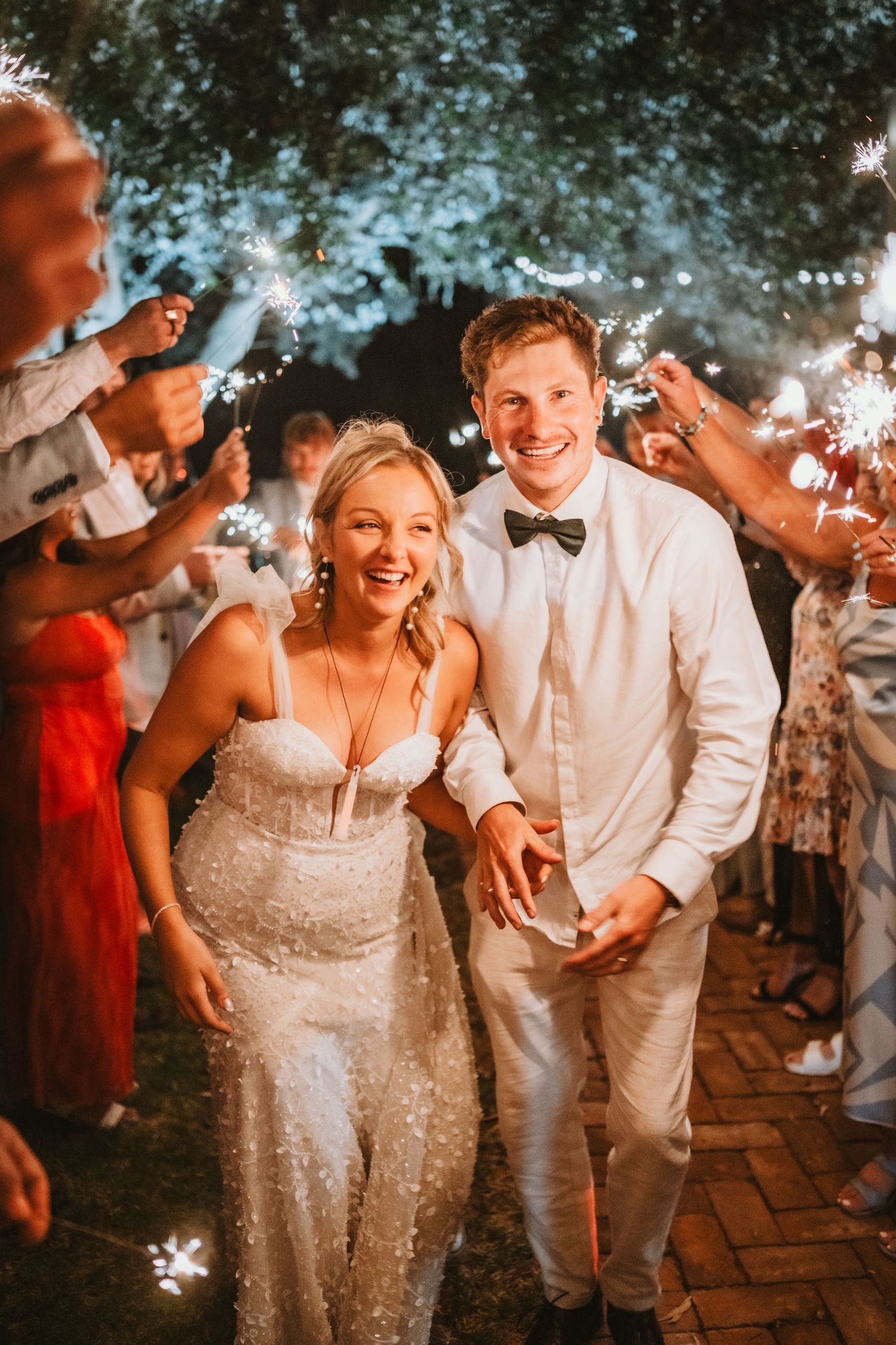Newlyweds celebrating with sparklers during their evening wedding reception on a brick pathway.