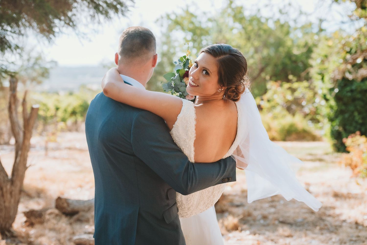 A couple in wedding attire embrace while dancing outdoors in a natural setting with mountains in the background.
