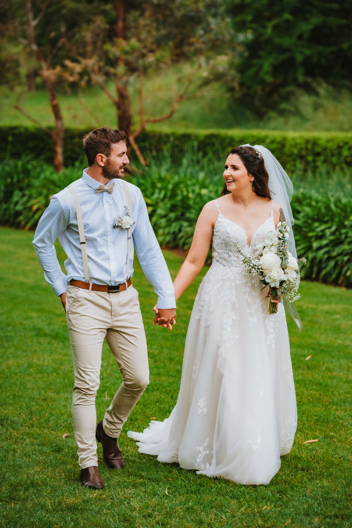 A newly married couple walks hand in hand on a lush green lawn during their outdoor garden wedding celebration.