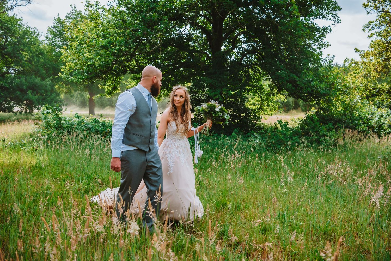A couple walks together through a lush summer meadow during a romantic outdoor wedding photoshoot.