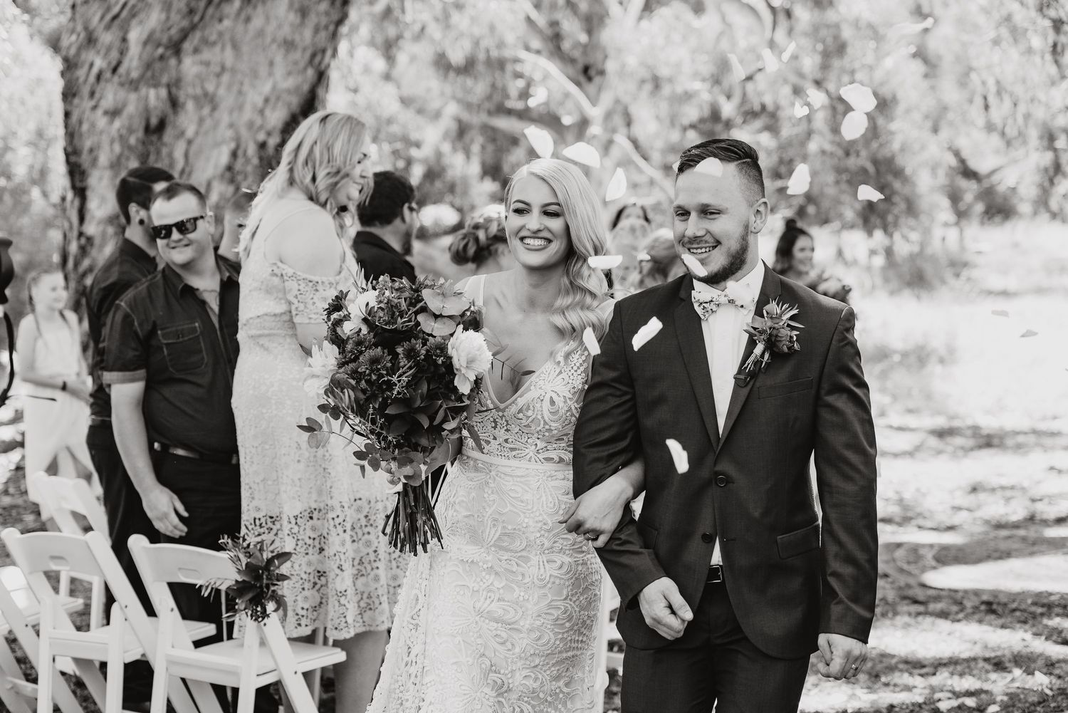 A couple joyfully walks back down the aisle at an outdoor wedding ceremony while guests celebrate.