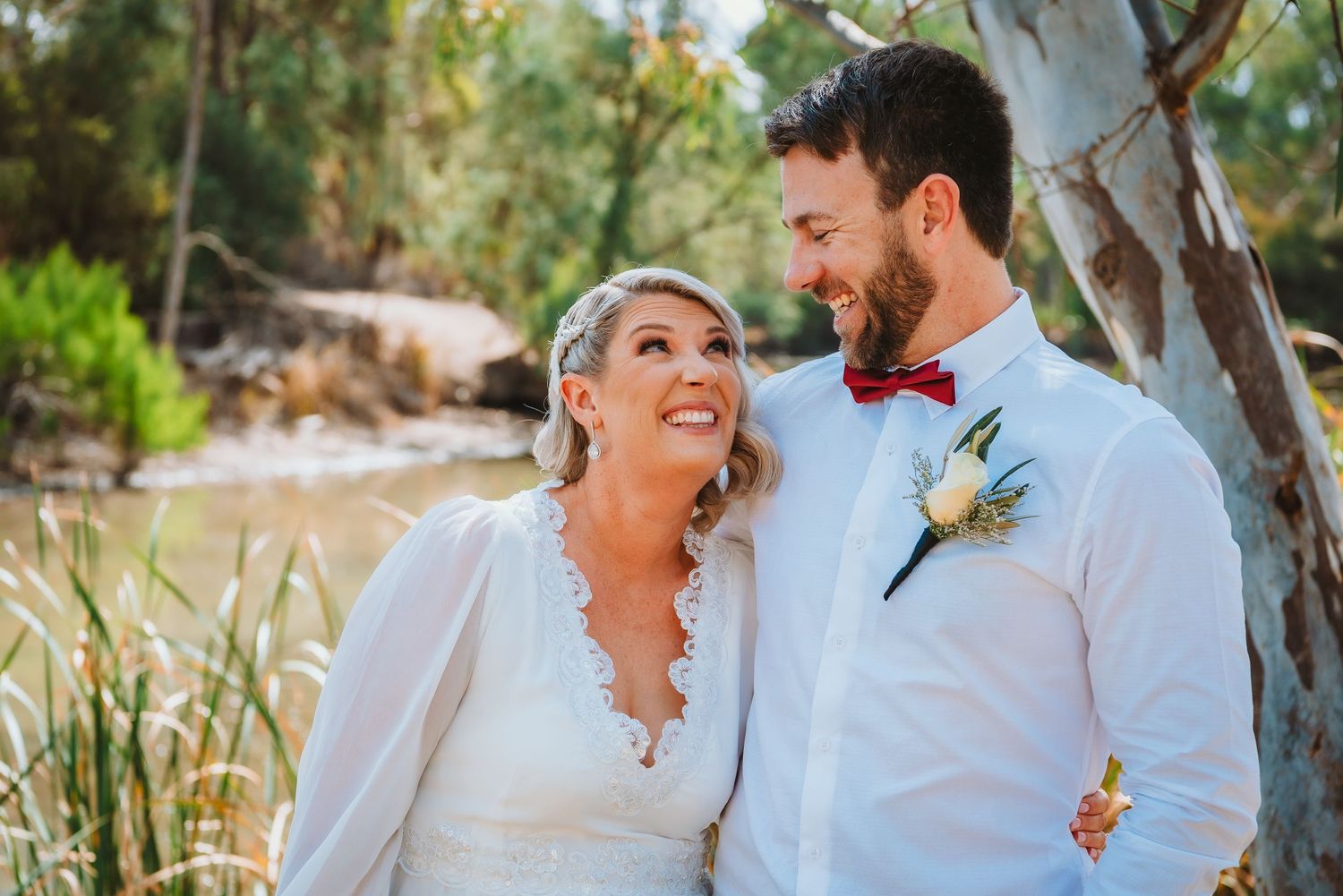 Wedding couple shares a joyful moment together outdoors in a natural garden setting with eucalyptus trees.